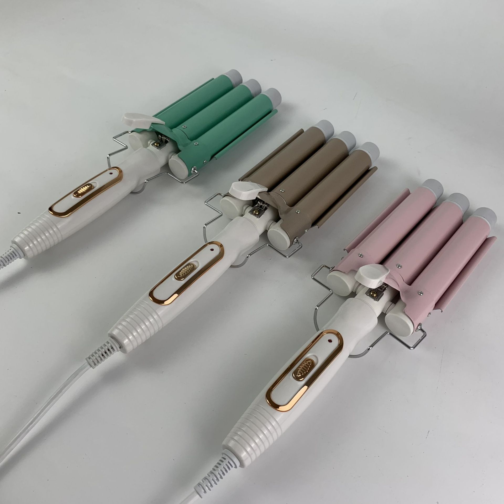 Drei Haarwellengeräte in Grün, Braun und Rosa. Sie haben weiße Griffe und ein wellenförmiges Design.
