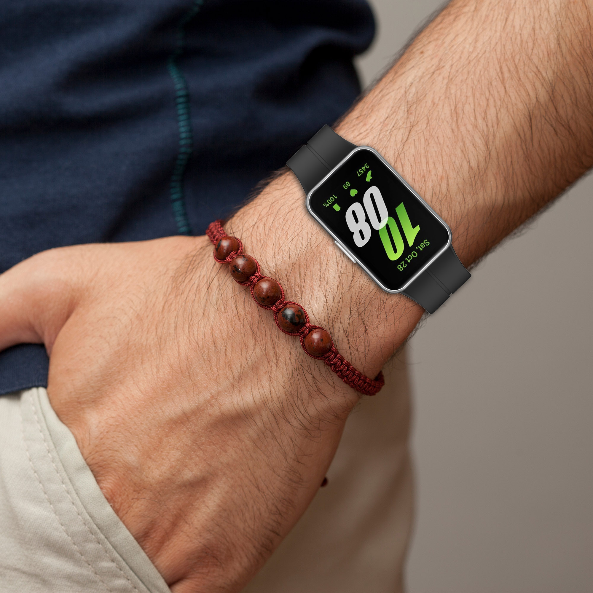 Handgelenk mit schwarzer Smartwatch, die Zeit und Statistiken anzeigt. Rotes Perlenarmband.