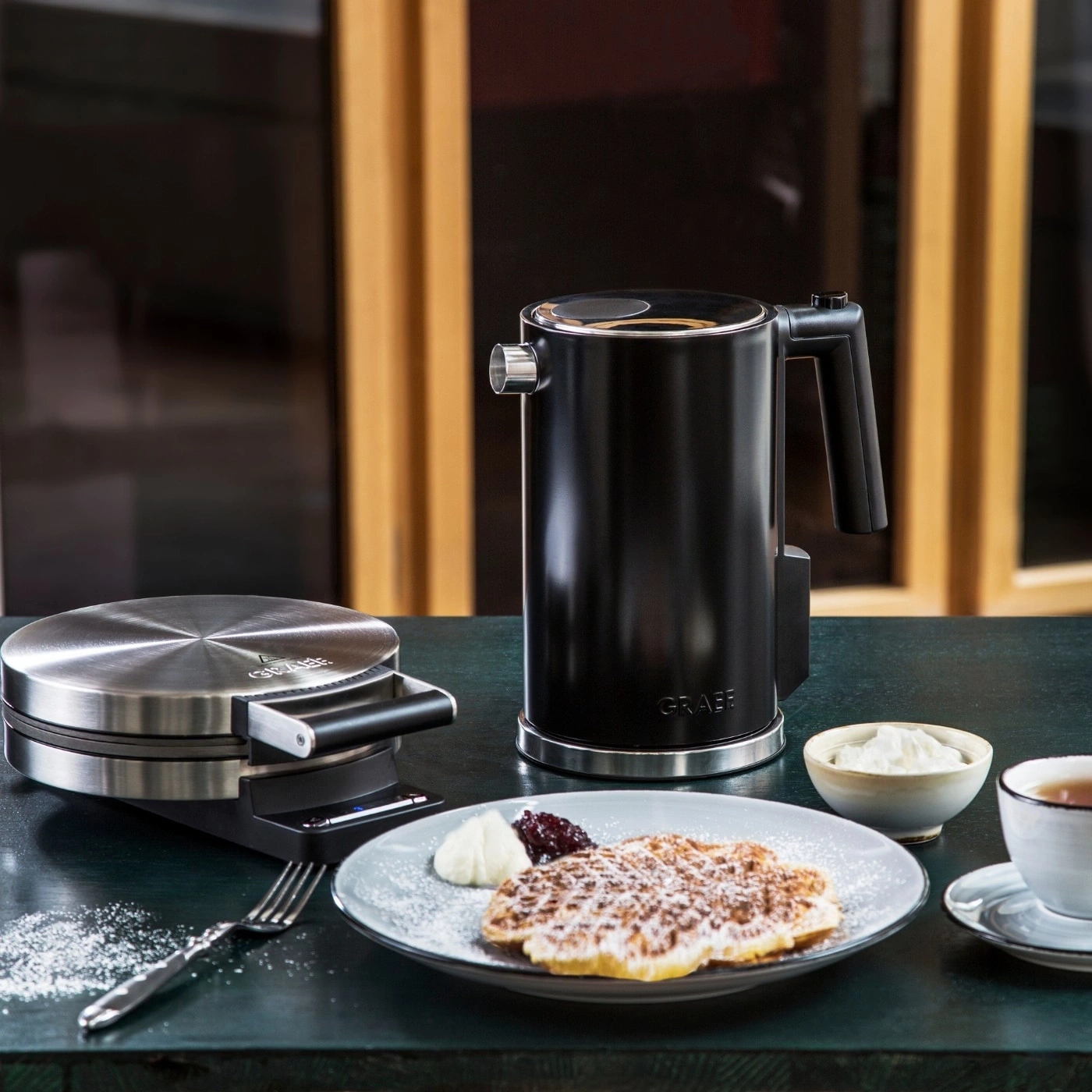 Scena kuchenna z gofrownicą, czajnikiem, goframi z dodatkami i filiżanką herbaty.