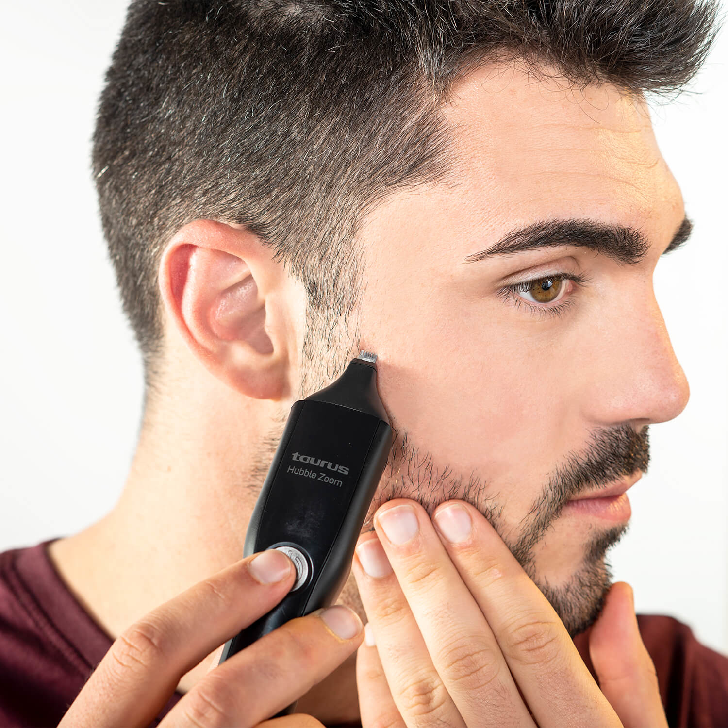 Un uomo si rade la barba con un trimmer nero. Tiene il trimmer sulla guancia.