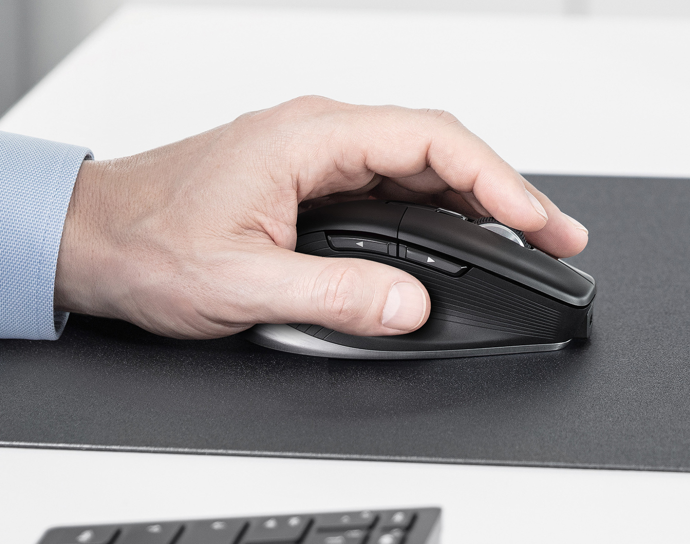 Een hand die een zwarte computermuis op een zwart bureaublad vasthoudt, toetsenbord is zichtbaar.