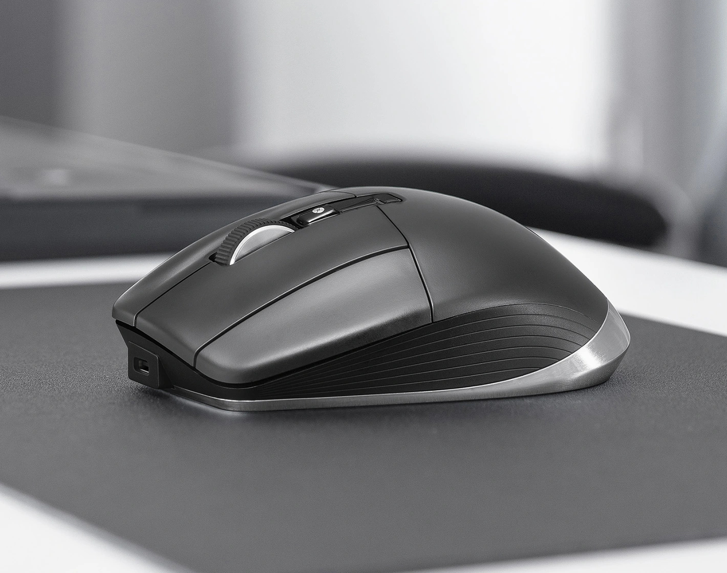 Een zwarte computermuis op een zwart muismatje. Een laptop is lichtjes wazig op de achtergrond.