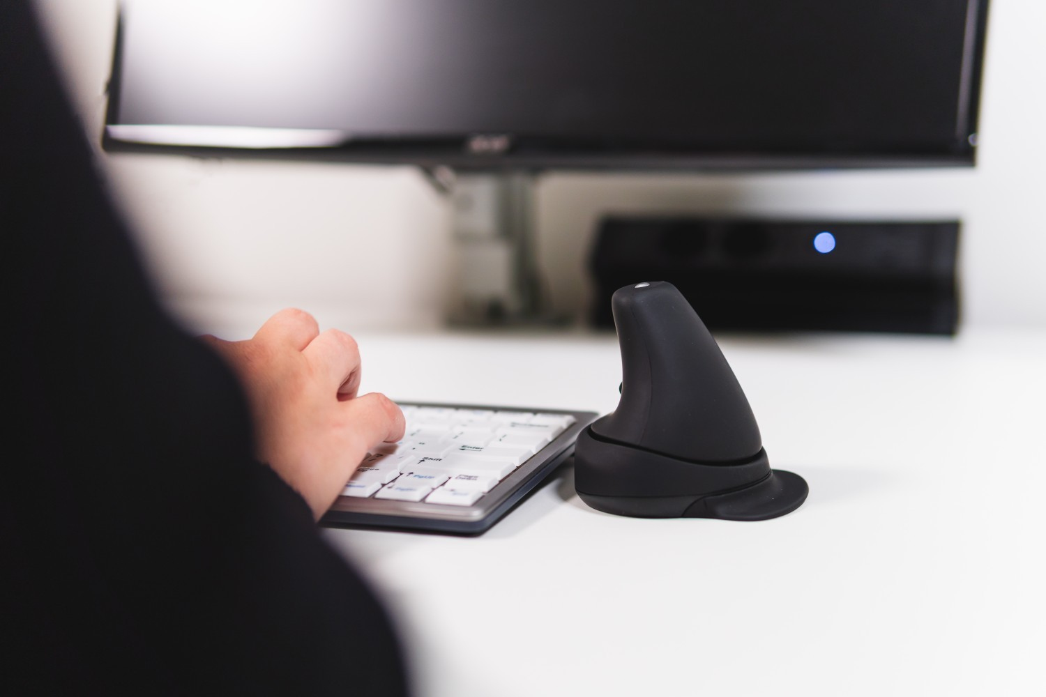 Persona che digita su una tastiera bianca, con un mouse ergonomico verticale nero a destra.