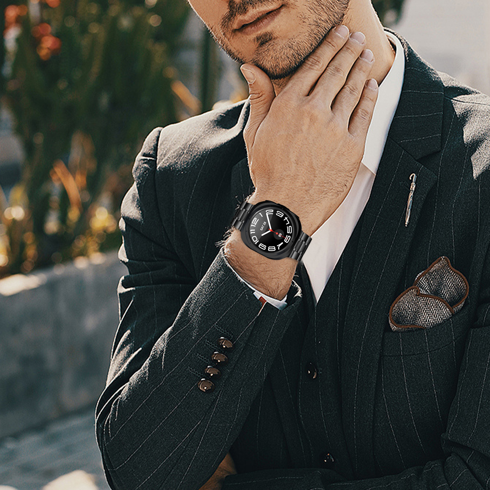 Ein Mann mit einer schwarzen Uhr mit schwarzem Armband. Er trägt einen Anzug und hält seine Hand an sein Gesicht.