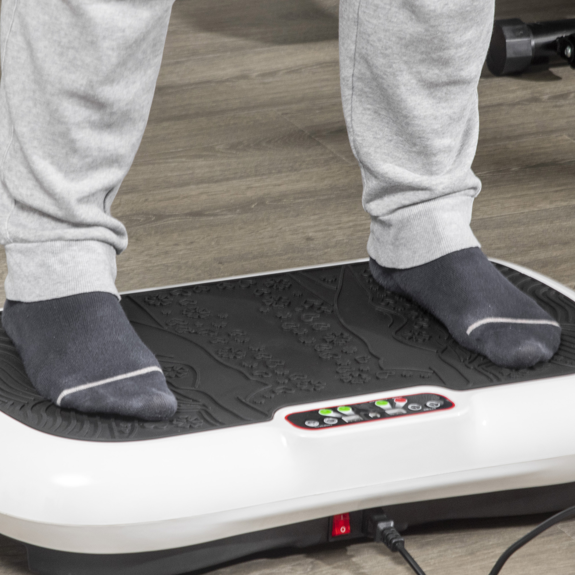 Person steht auf einer vibrierenden Trainingsplattform, trägt graue Jogginghose und Socken.