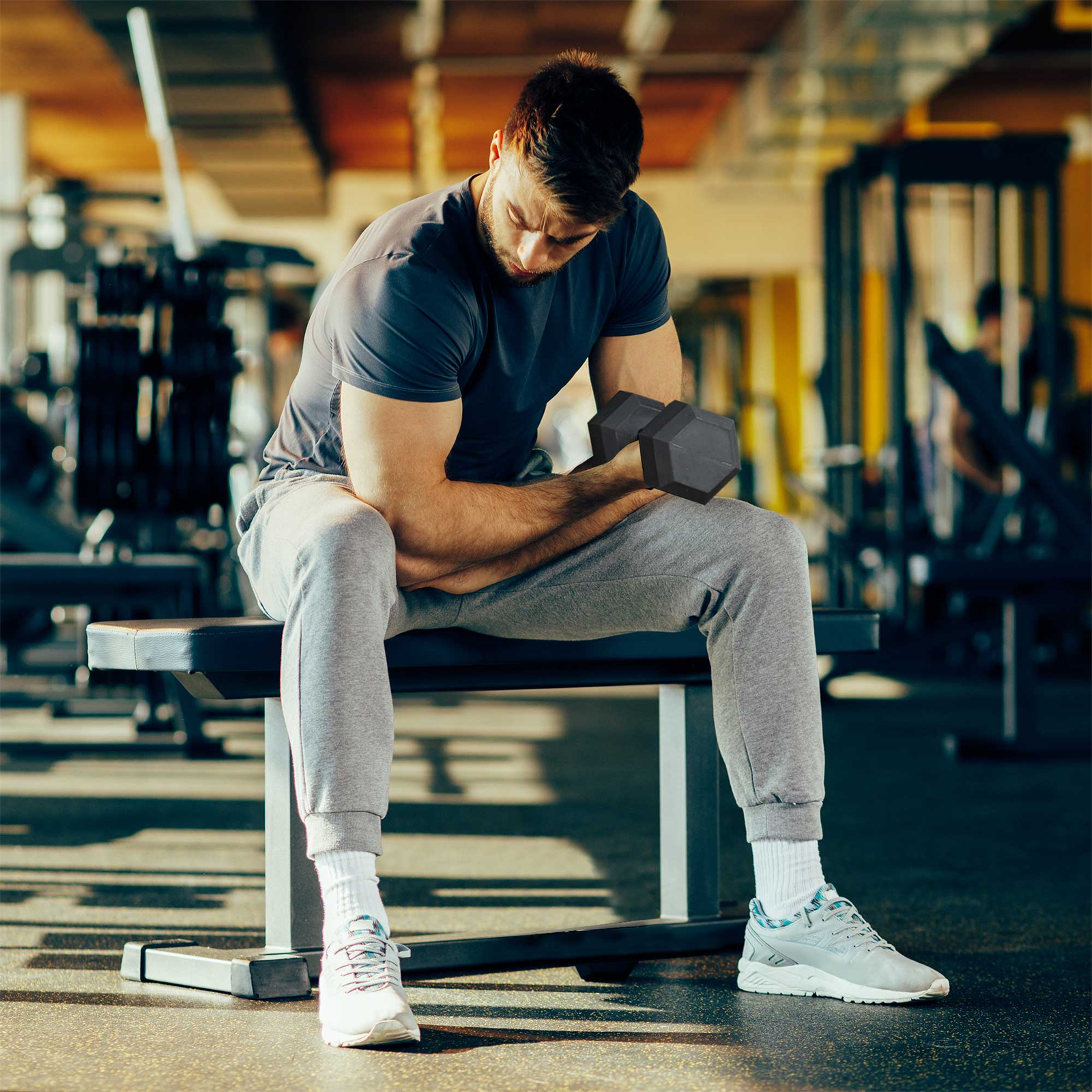 Ein Mann sitzt auf einer Bank in einem Fitnessstudio und hält eine Hantel, die sich auf ein Training konzentriert.