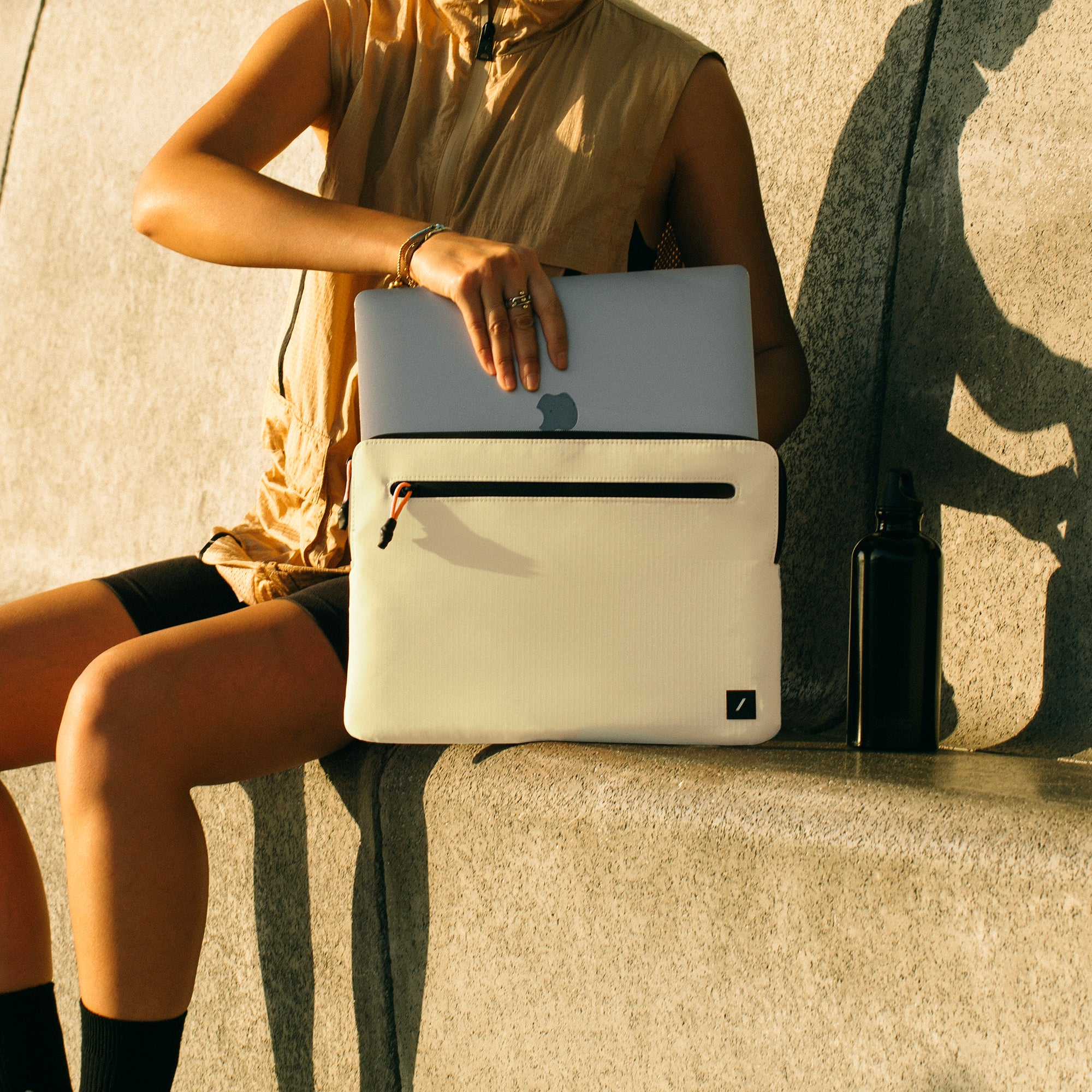 Persona che tiene un laptop grigio e una custodia. La custodia è beige con una cerniera nera.