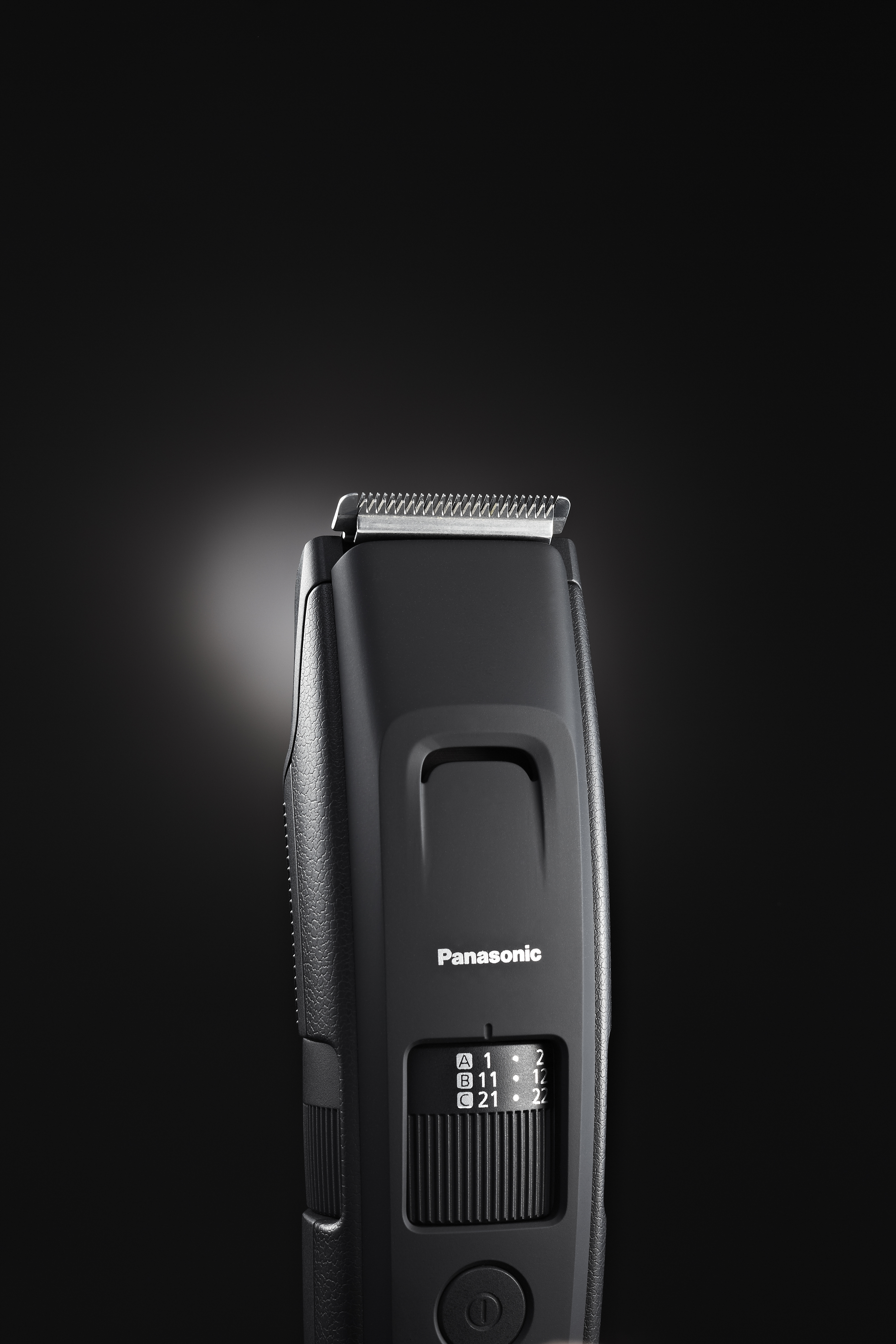 Tagliacapelli Panasonic nero, con quadrante delle impostazioni. Sfondo scuro con luce sopra il tagliacapelli.