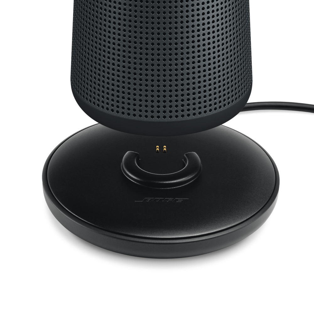 Ein schwarzer Lautsprecher auf einer schwarzen Ladestation, mit dem Bose-Logo sichtbar.