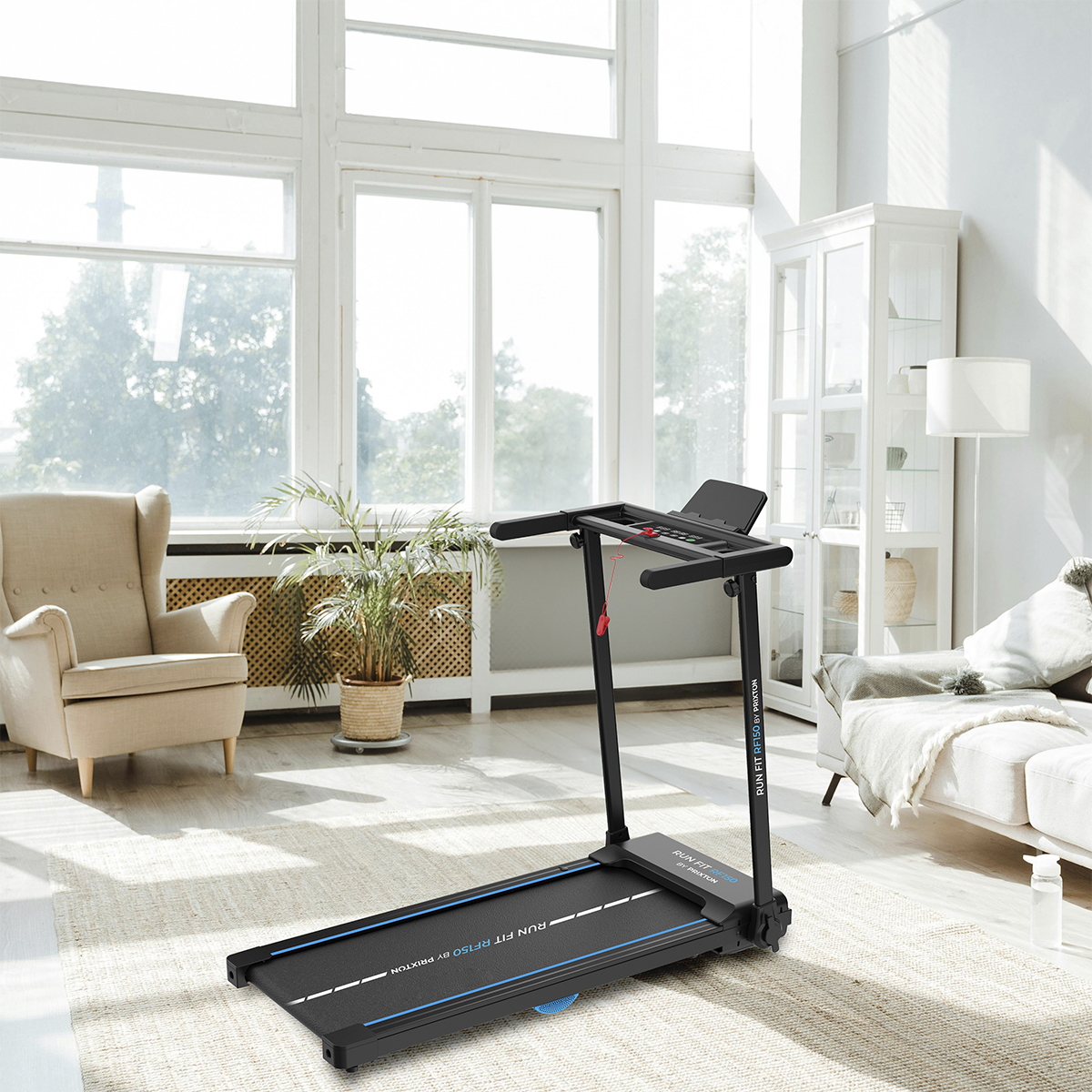 Wnętrze domu z bieżnią na pierwszym planie. Sofa, rośliny i duże okna w tle.