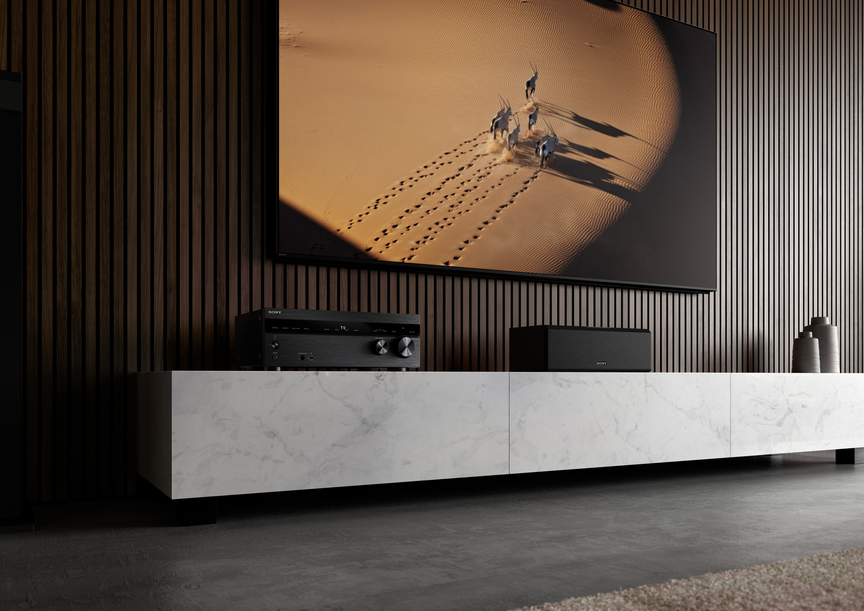 Wohnzimmer mit Marmormöbeln und großem Fernseher. Eine Soundbar und Lautsprecher darunter.