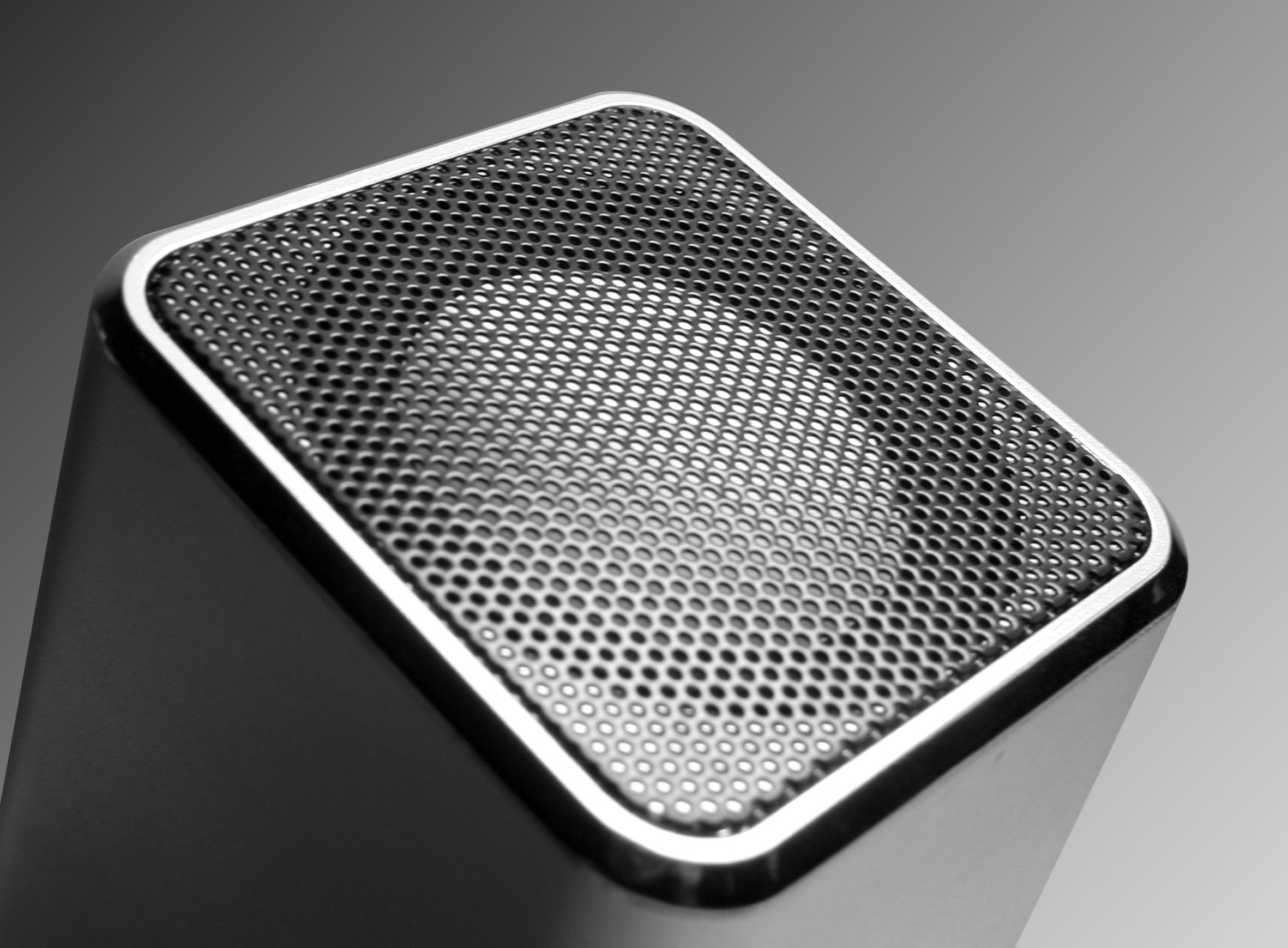 Zbliżenie szarego głośnika. Głośnik ma perforowaną metalową kratkę.