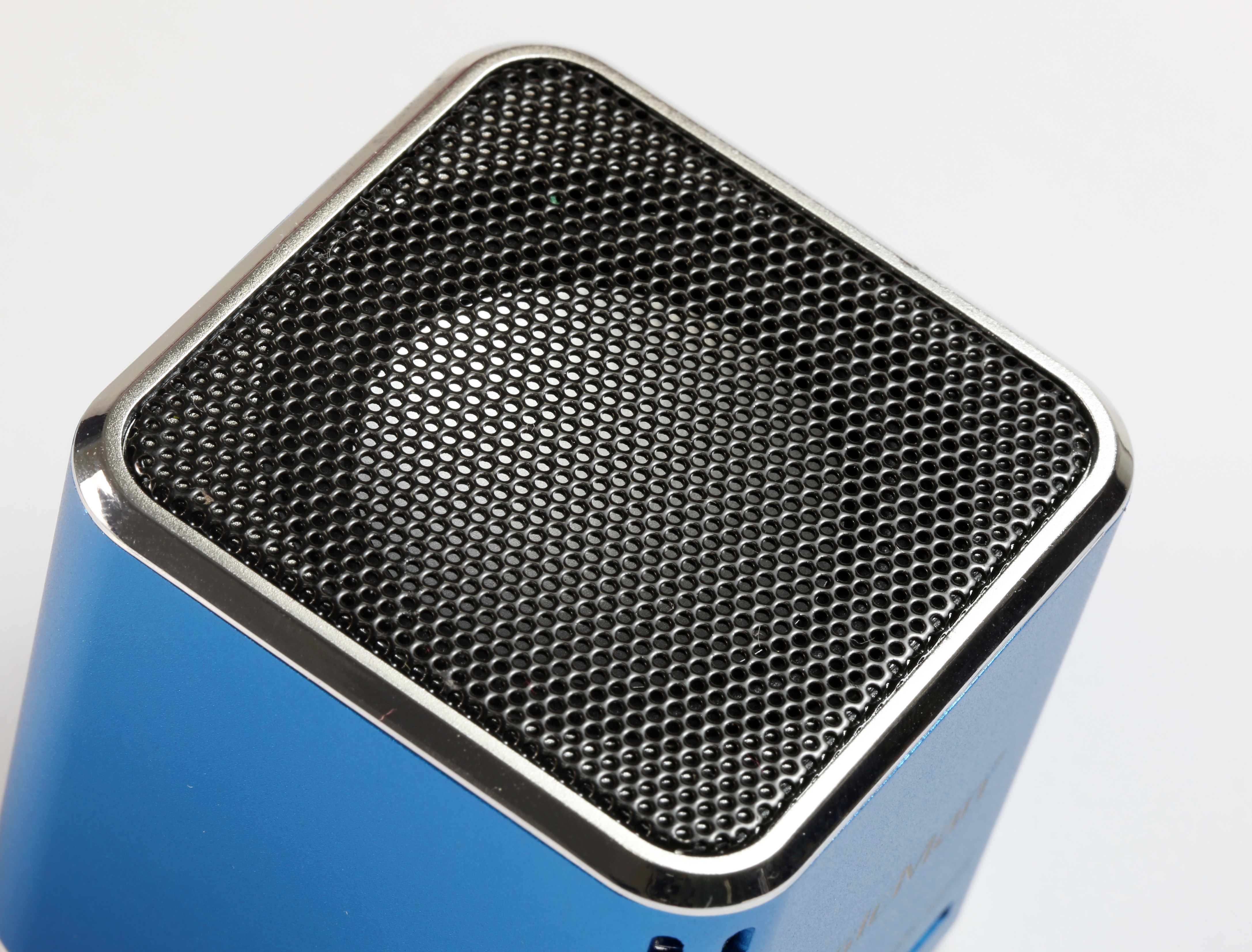 Niebieski głośnik z siatkowym przodem i srebrną obwódką na białym tle.