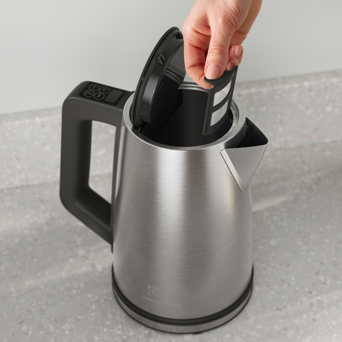 Ręka otwiera pokrywę czajnika ze stali nierdzewnej z filtrem w środku.