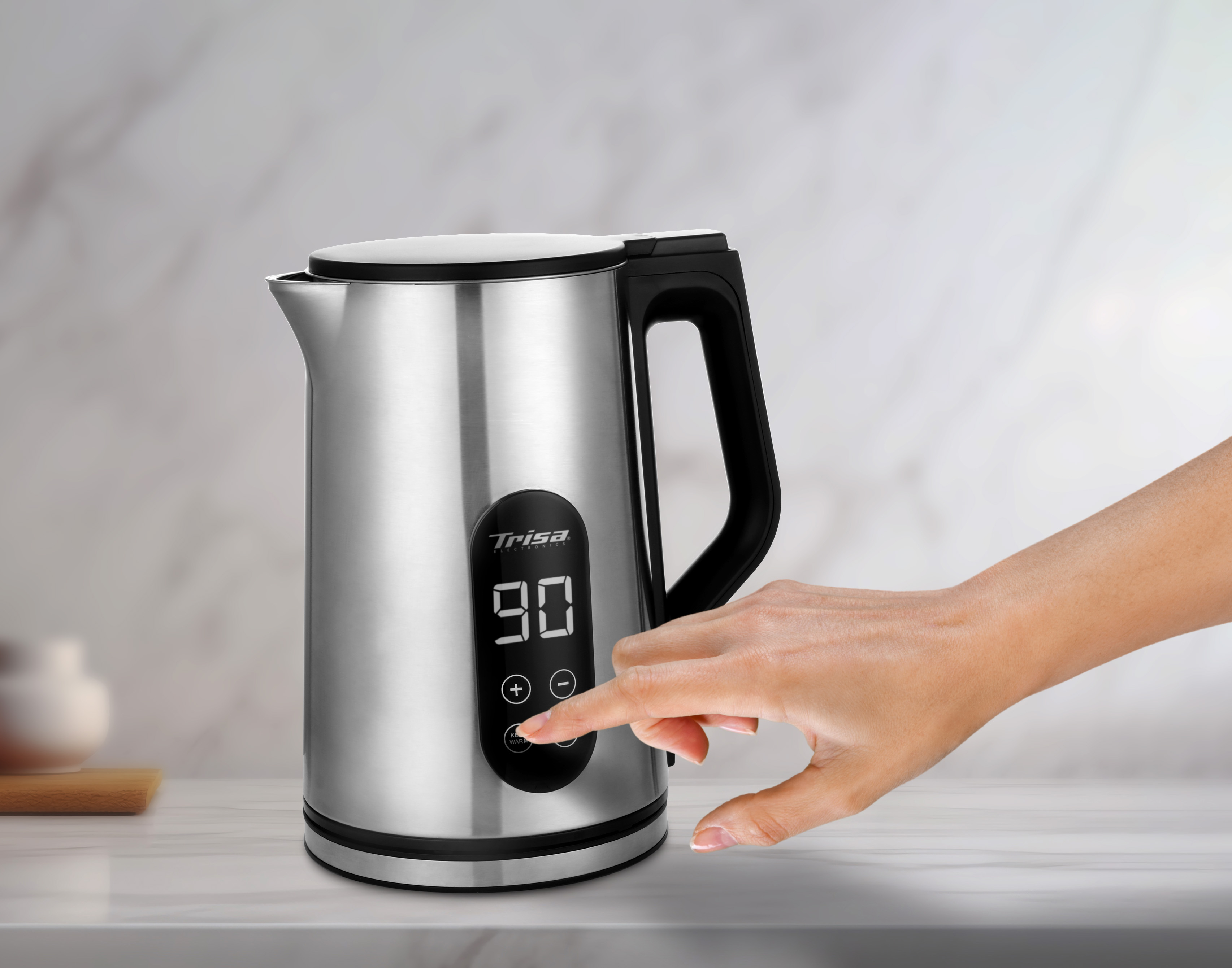 Bollitore elettrico argentato con manico nero, display che mostra 90 e mano che tocca i pulsanti.