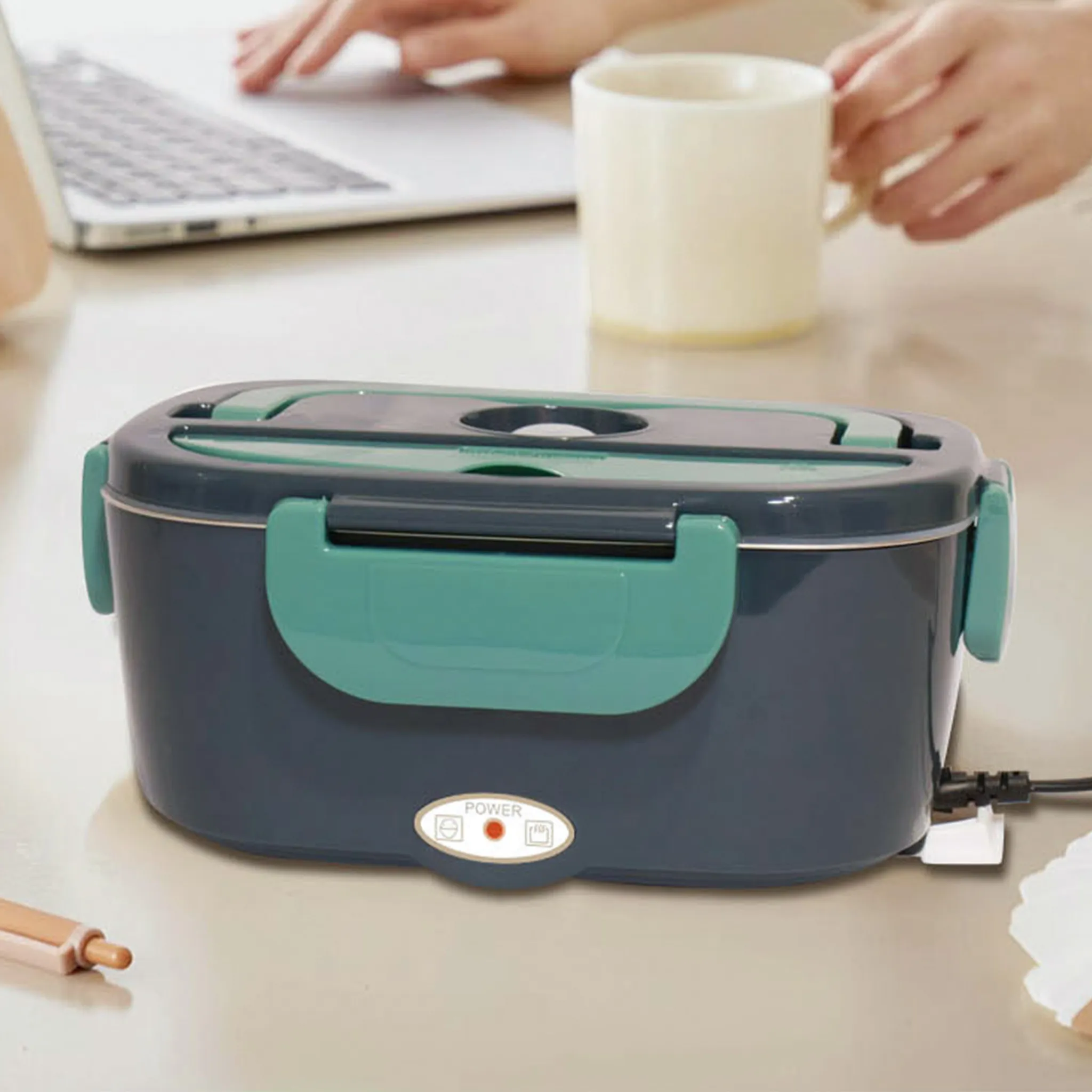 Beheizte Lunchbox auf dem Tisch. Hände, Laptop und Becher sind sichtbar.