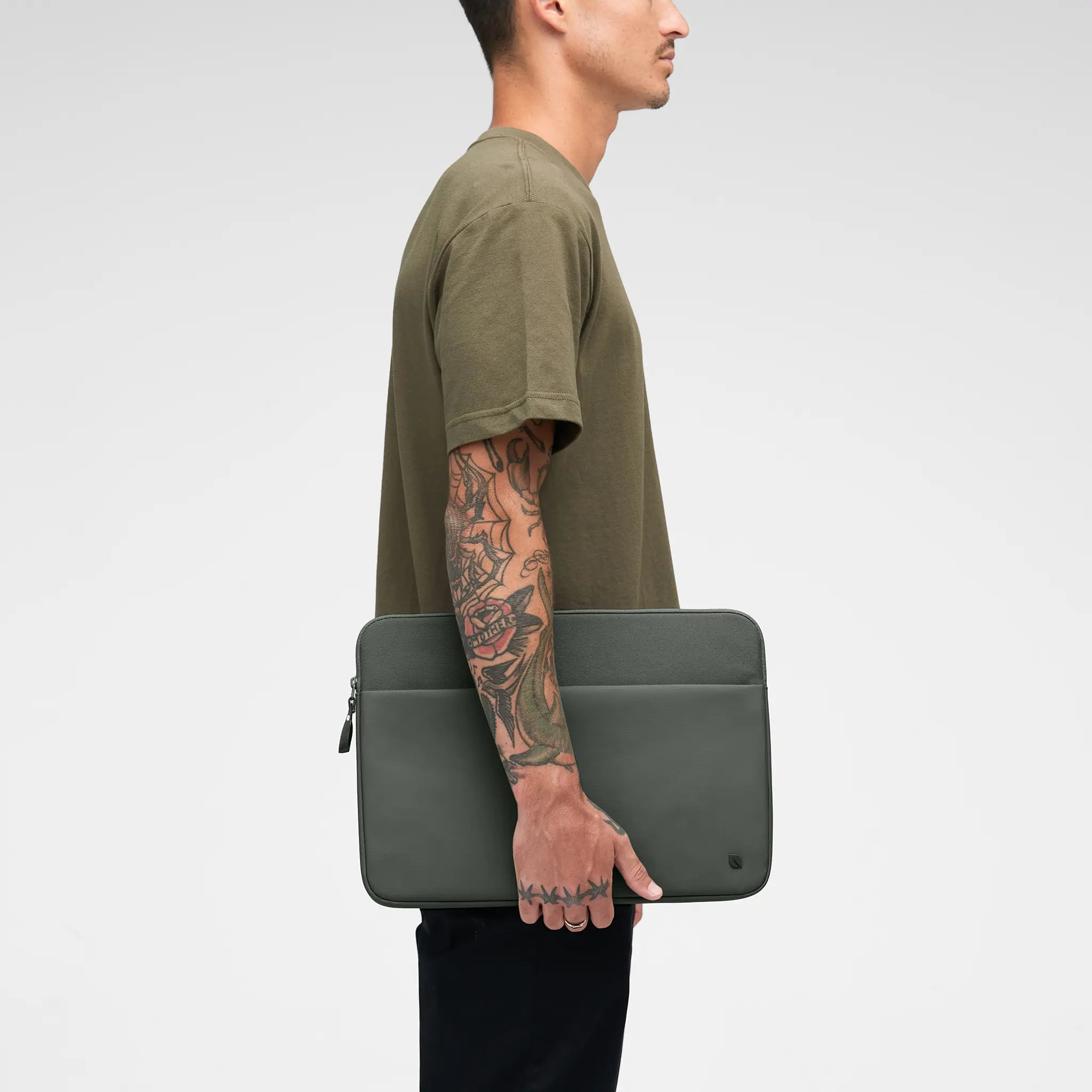 Uomo con custodia verde per laptop. Ha un tatuaggio sul braccio e indossa una camicia verde e pantaloni neri.