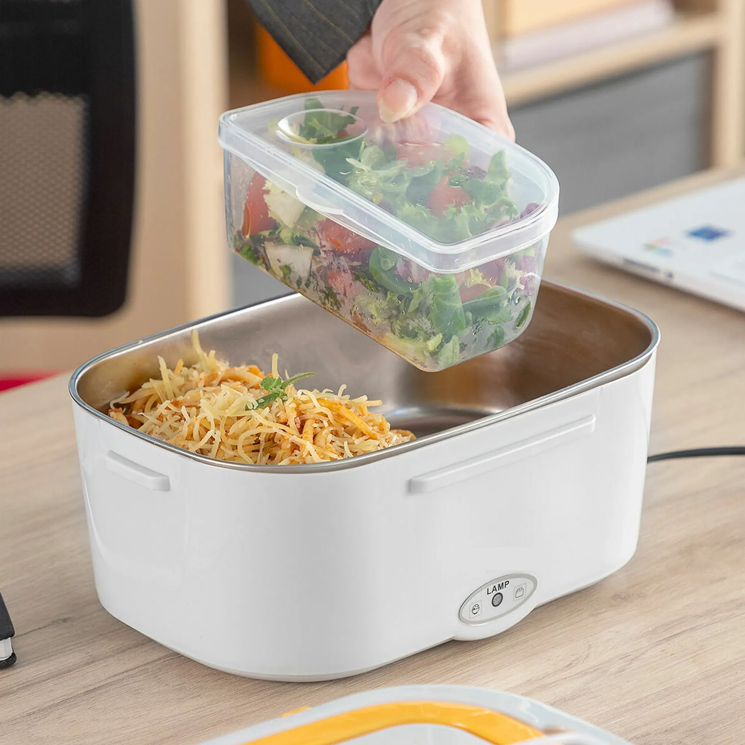 Eine Person legt einen Salatbehälter in eine beheizte Lunchbox.