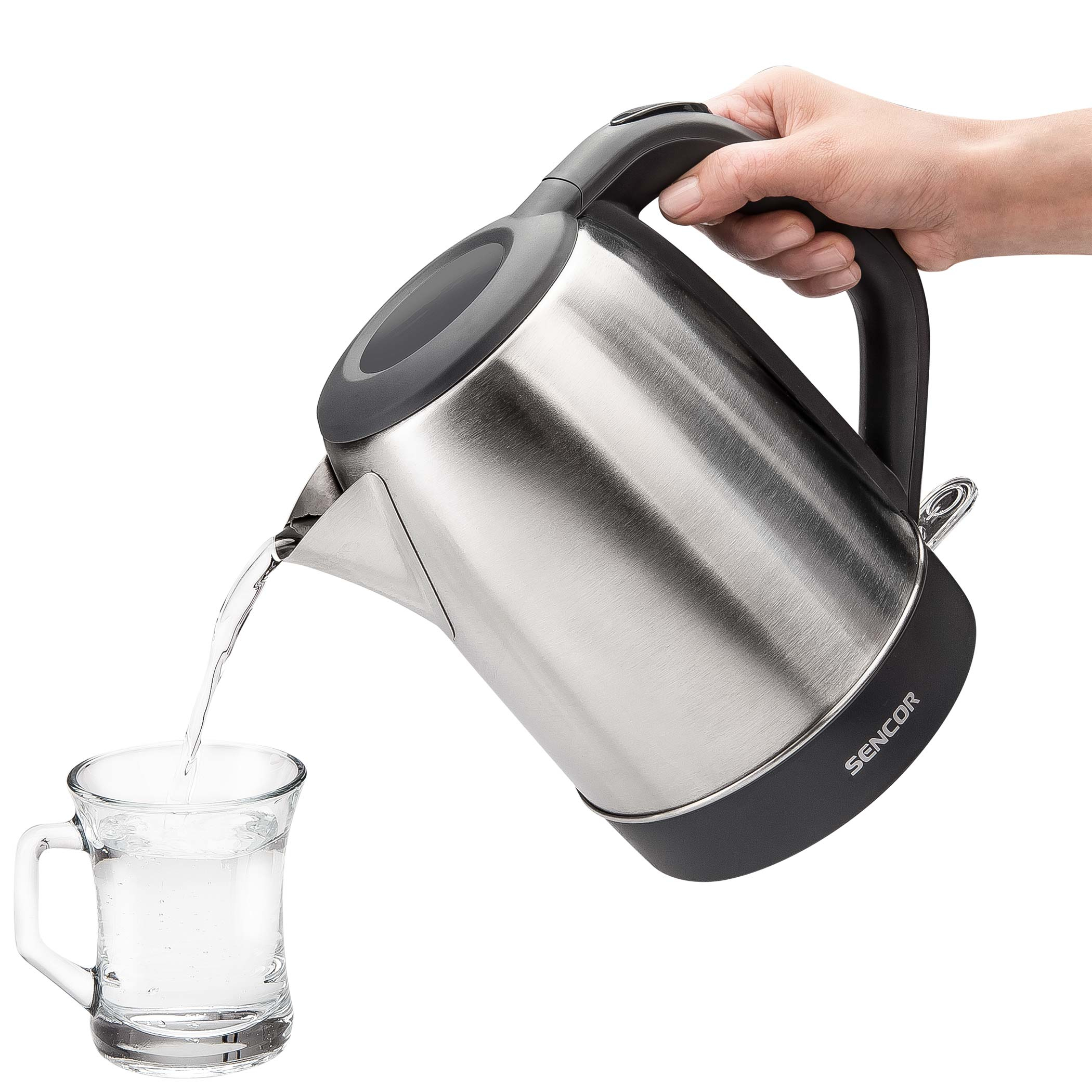 Een persoon giet water uit een zilveren waterkoker in een glas.