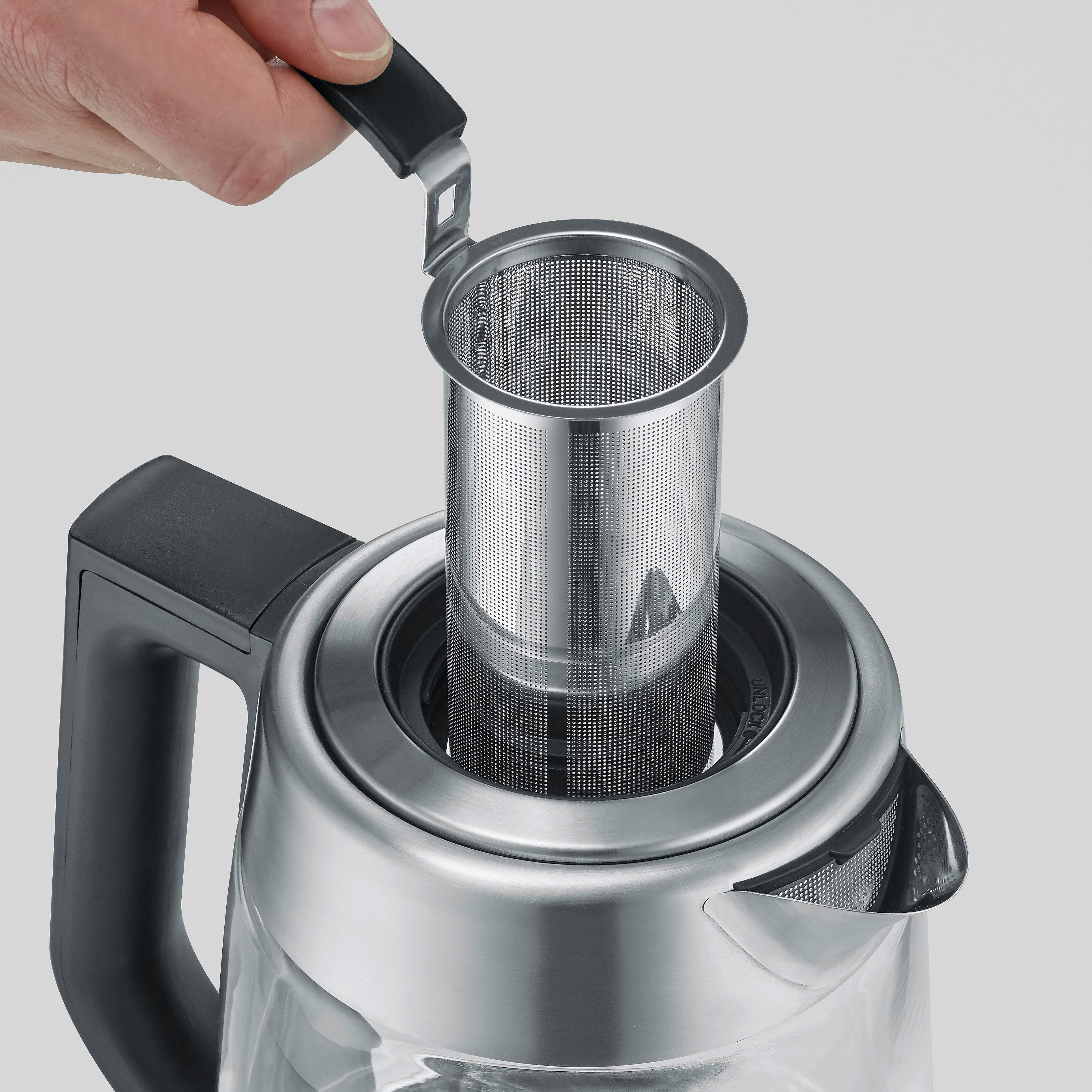 Una mano inserisce un infusore per tè in acciaio inossidabile in un bollitore in vetro trasparente.