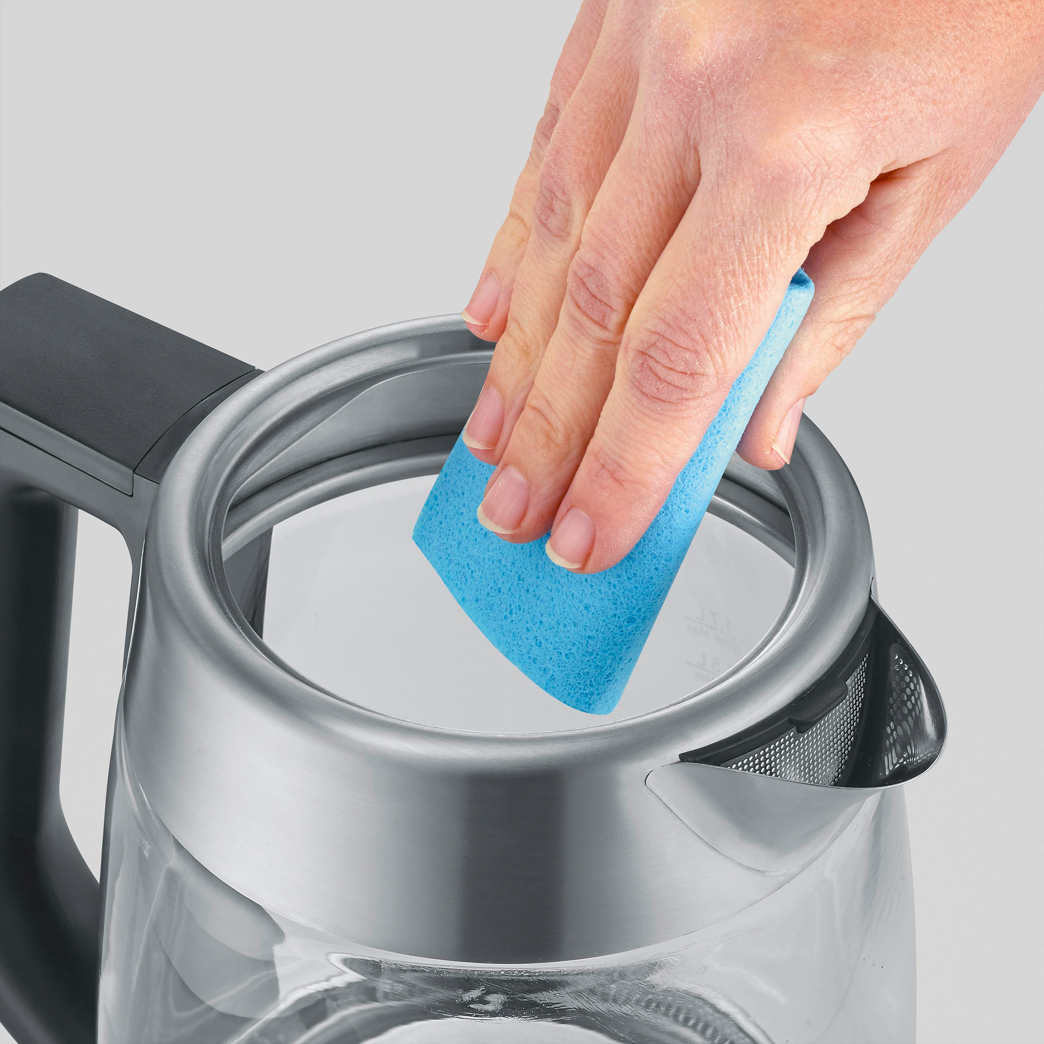 Una persona pulisce un bollitore di vetro con una spugna blu.