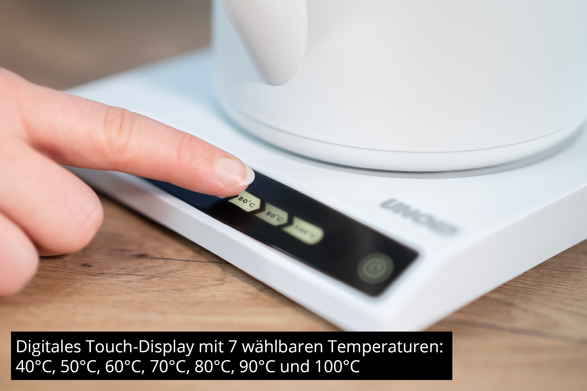 Eine Hand berührt die digitale Anzeige eines weißen Wasserkochers.