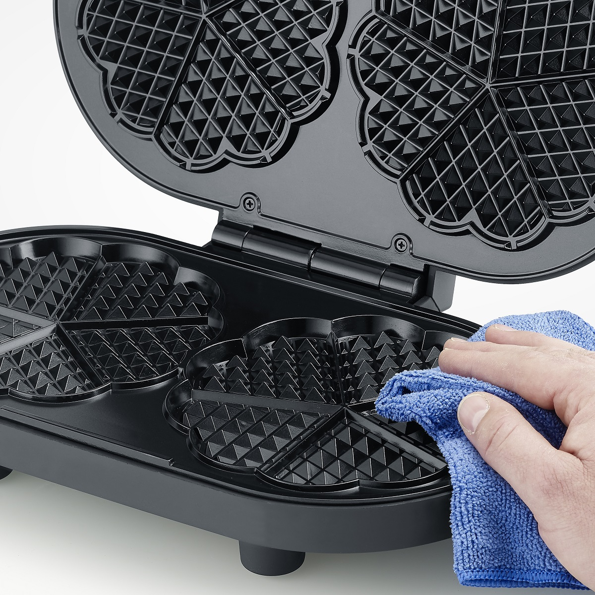 Eine Person reinigt einen Waffeleisen mit einem blauen Tuch.