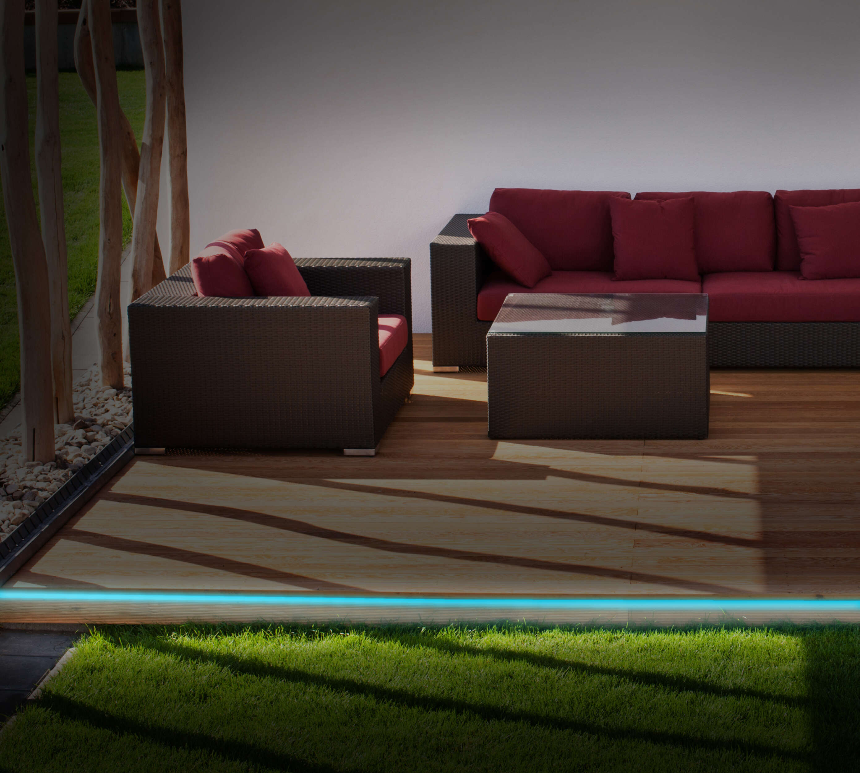 Eine Terrasse mit Couch und Stühlen, und ein blaues Licht am Boden entlang.
