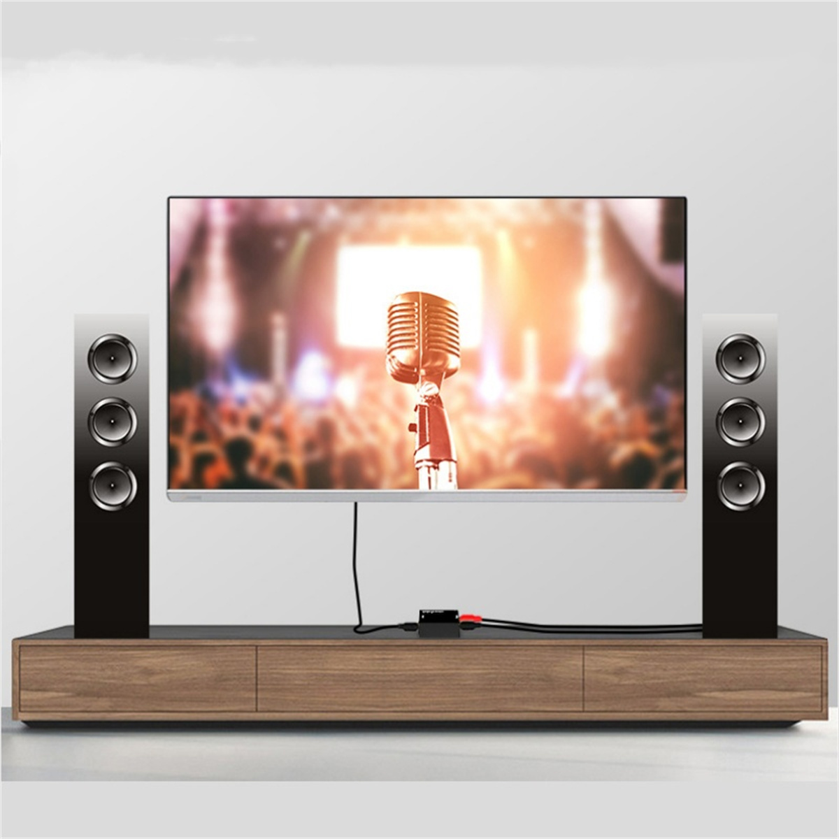 Fernseher mit Lautsprechern und Mikrofon auf einem Holzregal, mit Publikum im Hintergrund.