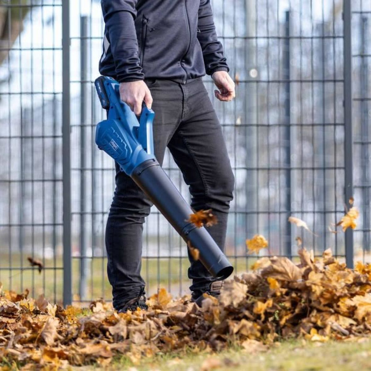 Ein Mann mit einem Laubbläser in einem Hof mit Blättern auf dem Boden.