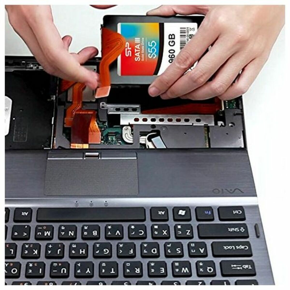 Ręce instalujące dysk SSD w laptopie. Laptop jest otwarty, widać jego wewnętrzne komponenty.