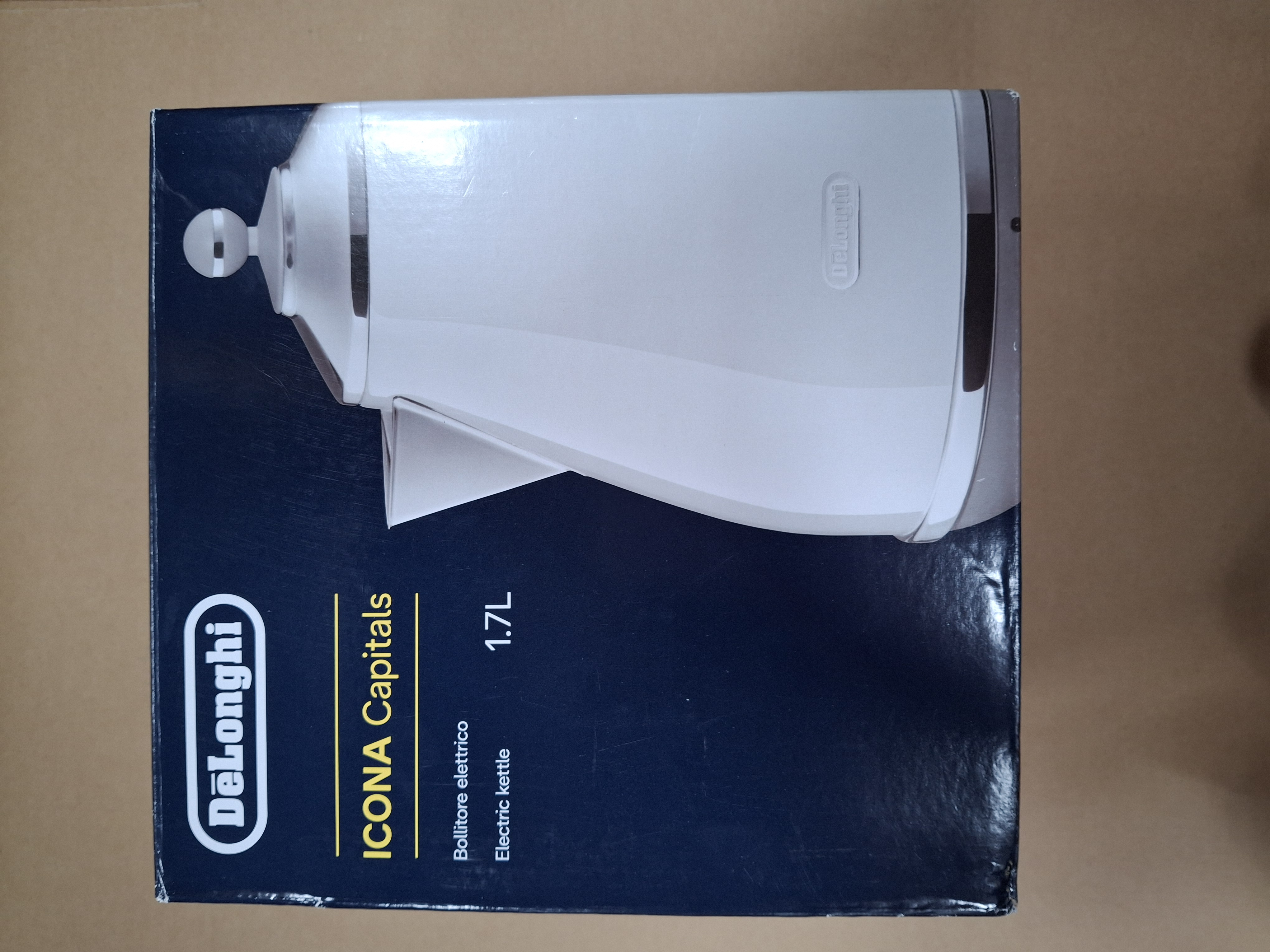 A white DeLonghi ICONA electric kettle in its box, with text and the kettle visible.