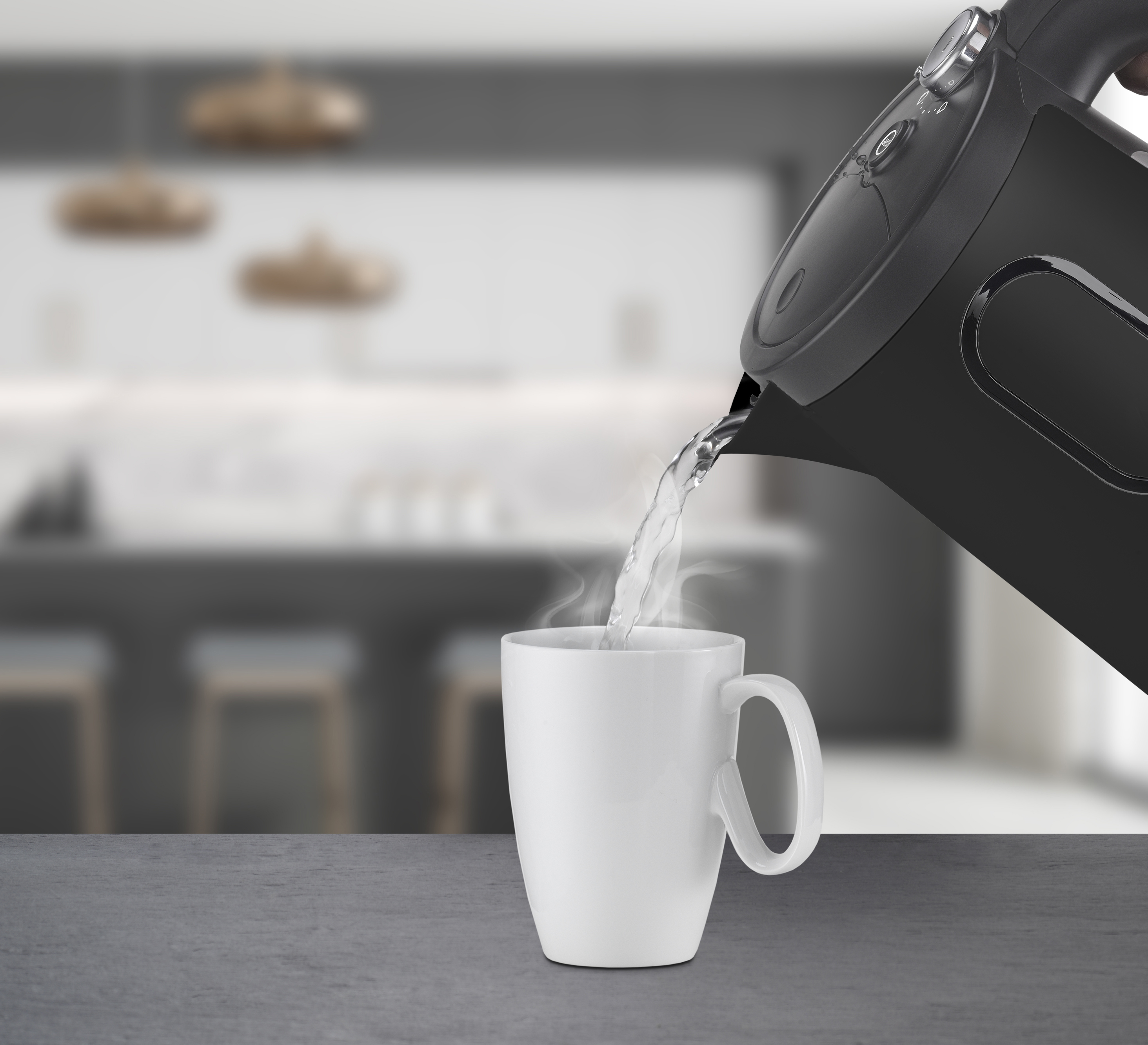 Ein schwarzer Wasserkocher gießt heißes Wasser in eine weiße Tasse auf einer grauen Arbeitsplatte.