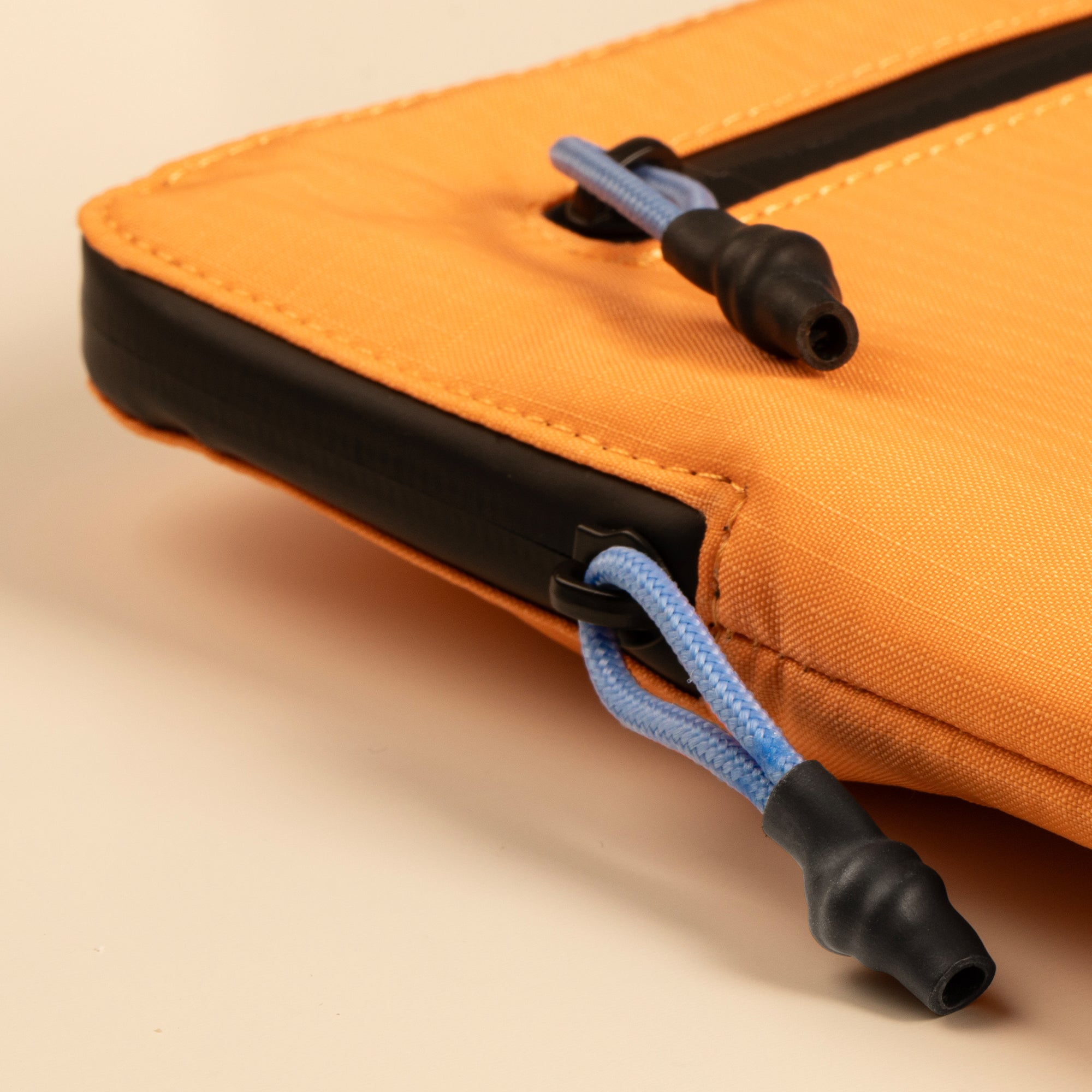 Nahaufnahme einer orangefarbenen Tasche mit schwarzen Akzenten und blauem Kordelzug. Beiger Hintergrund.