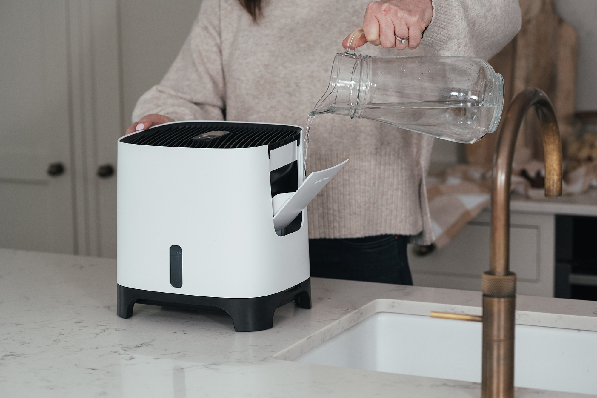 Osoba wlewa wodę do biało-czarnego oczyszczacza powietrza.