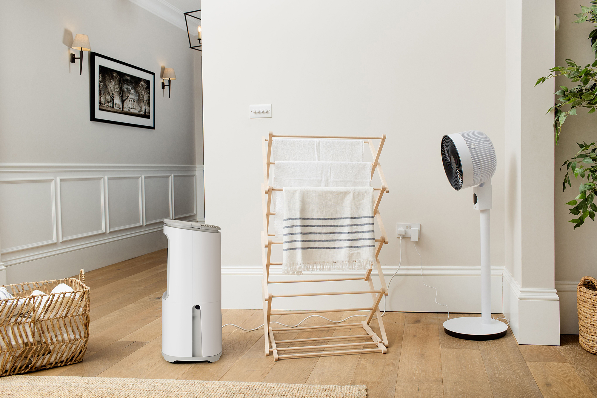 Ein Raum mit einem Luftentfeuchter, einem Wäscheständer mit Handtüchern, einem Ventilator und einem Korb.