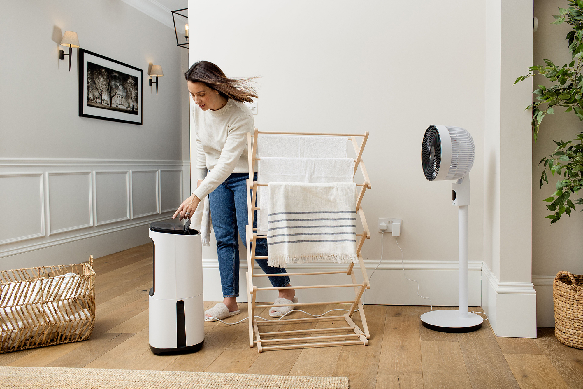 Kobieta używająca osuszacza i suszarki w jasnym pokoju, z wentylatorem.