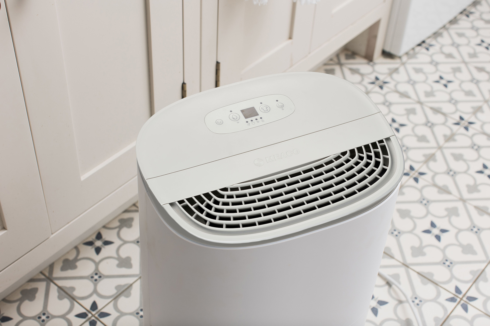 Witte luchtreiniger. Het heeft een ventilatieopening, een bedieningspaneel en staat op een vloer.