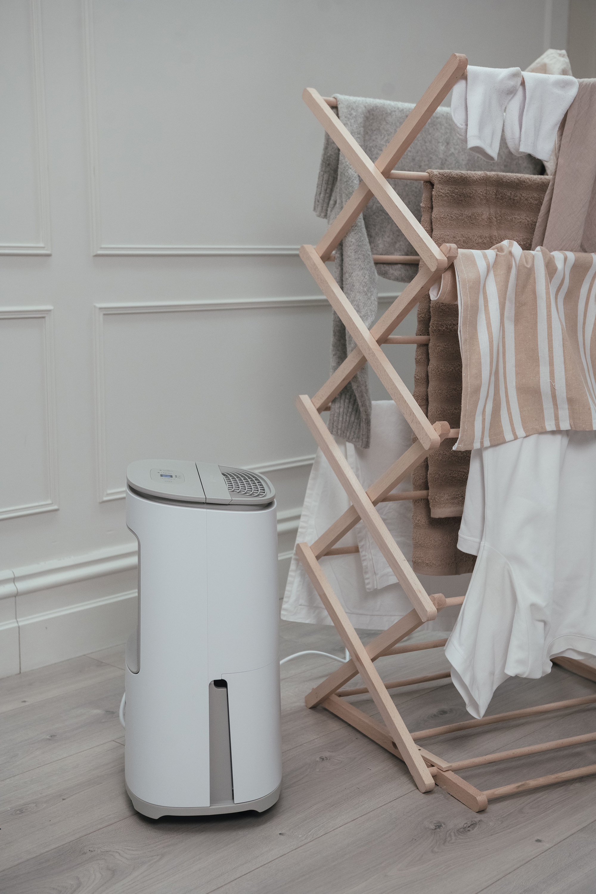 Een witte luchtontvochtiger en een houten droogrek met kleding in een kamer.