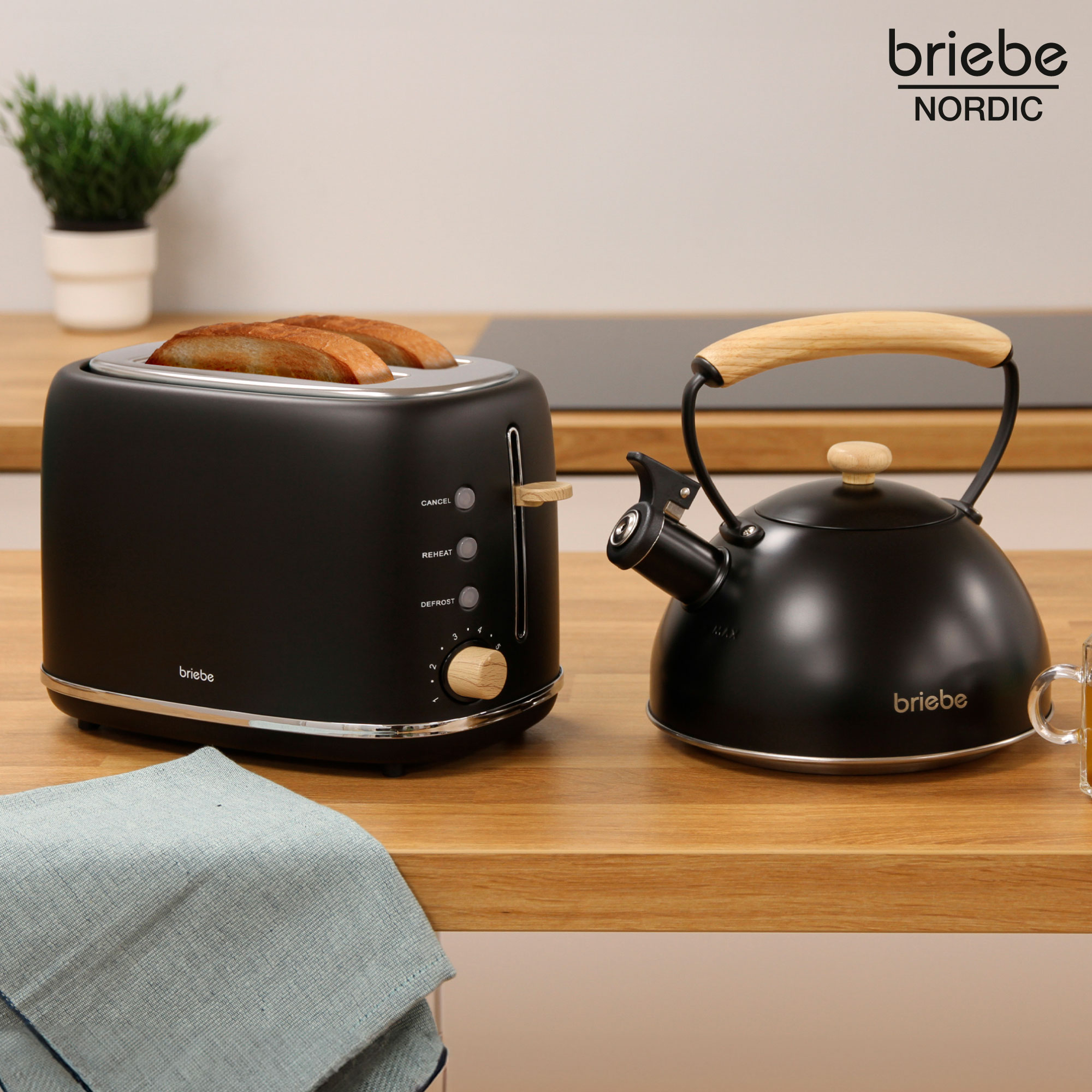 Ein schwarzer Toaster mit Brot und ein Wasserkocher auf Holzoberfläche mit grünem Tuch.