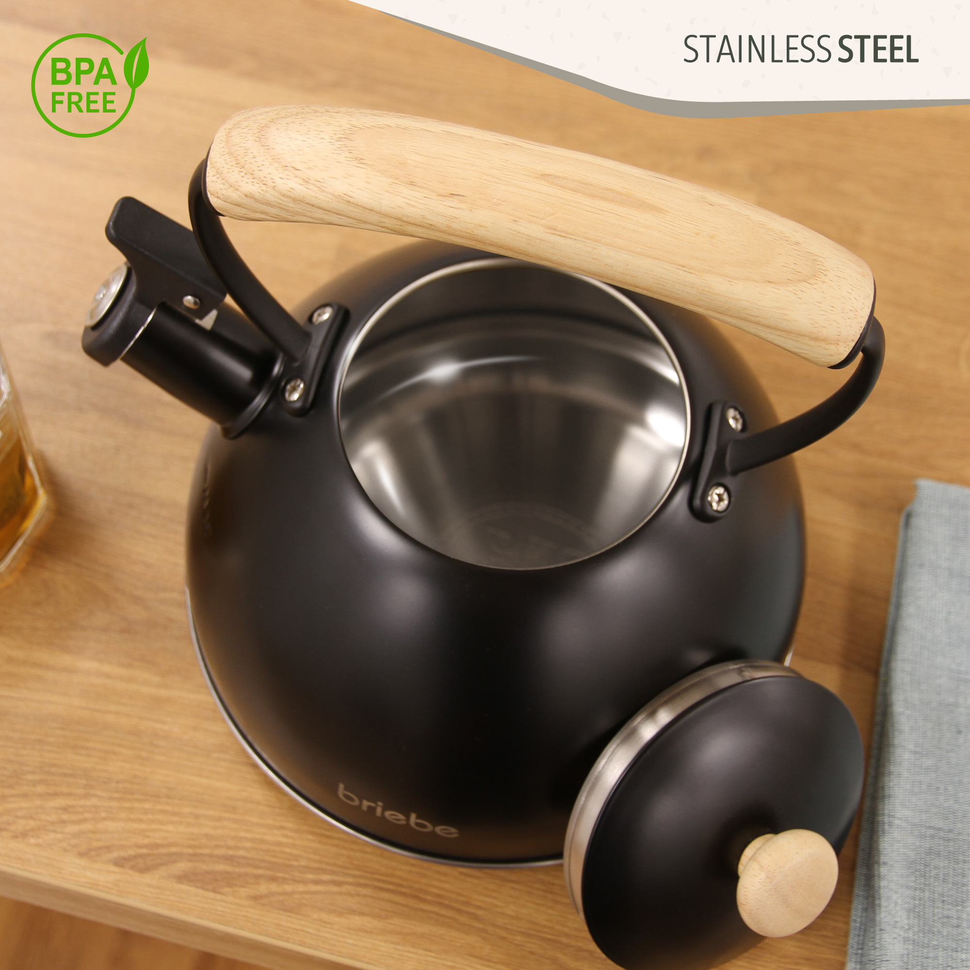 Schwarzer Wasserkocher mit Holzgriff. Offener, Edelstahl-Innenraum. 'BPA FREE' und 'STAINLESS STEEL' Etiketten.