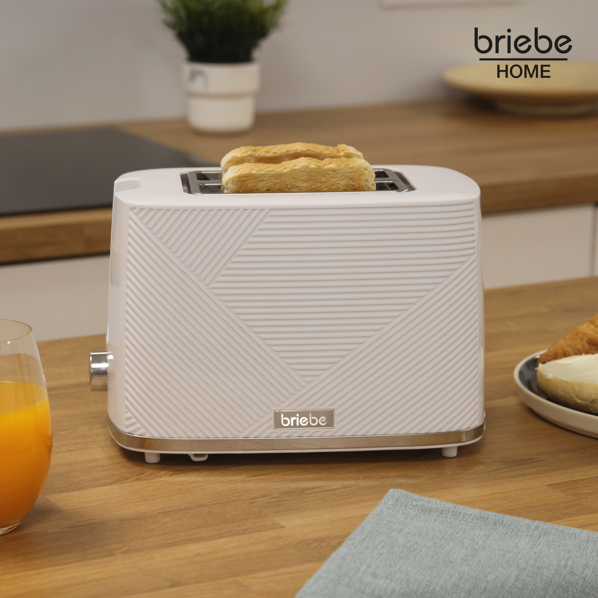 Weißer Toaster mit Toast, Orangensaft und Serviette auf einem Holztisch.