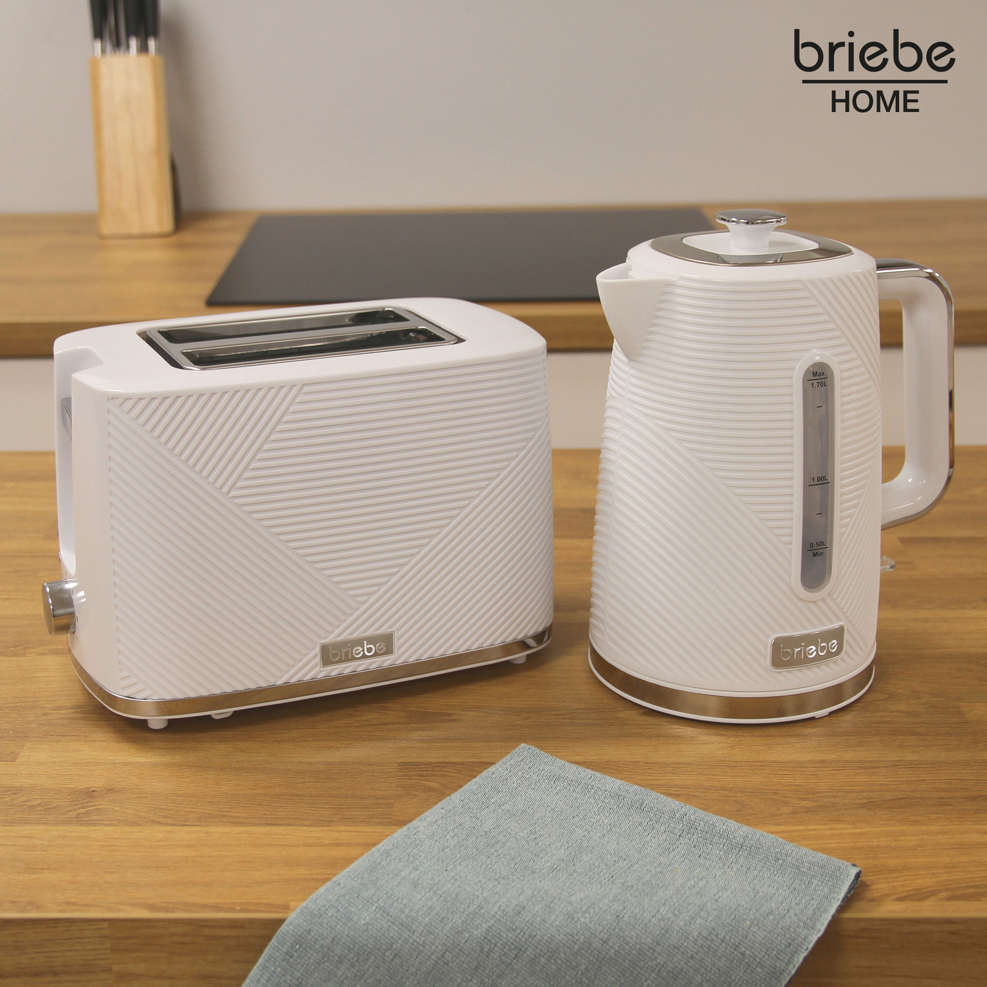 Ein weißes Toaster- und Wasserkocher-Set auf einer Holzoberfläche neben einem blauen Tuch. Die Marke ist briebe.