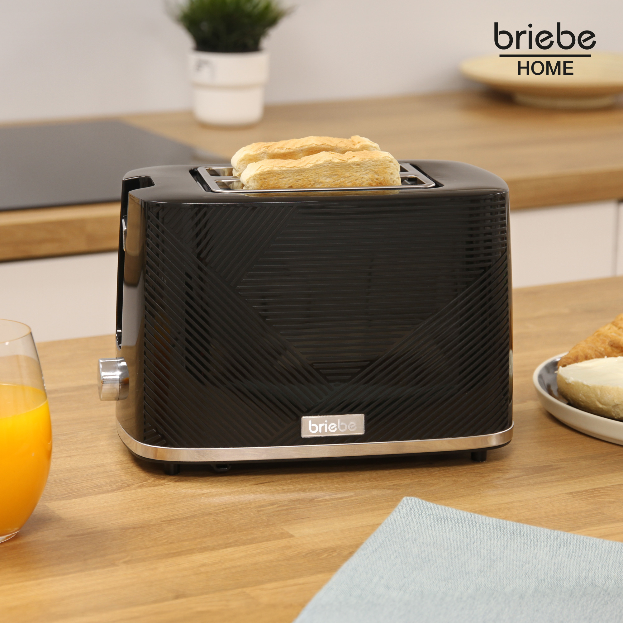 Schwarzer Toaster mit Toast und ein Glas Orangensaft auf Holzplatte.