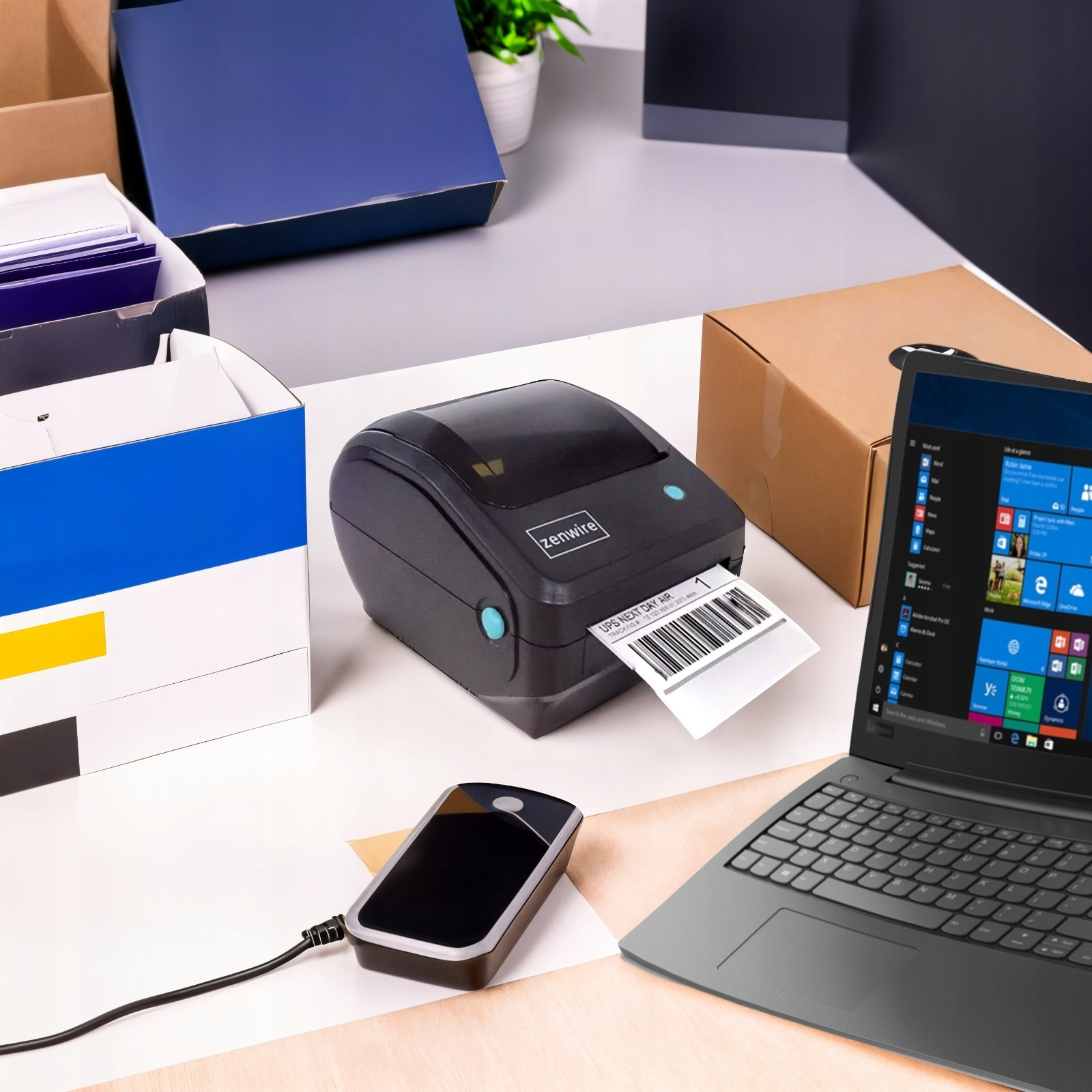 Drukarka drukująca etykietę. Inne elementy: laptop, pudełka i telefon.