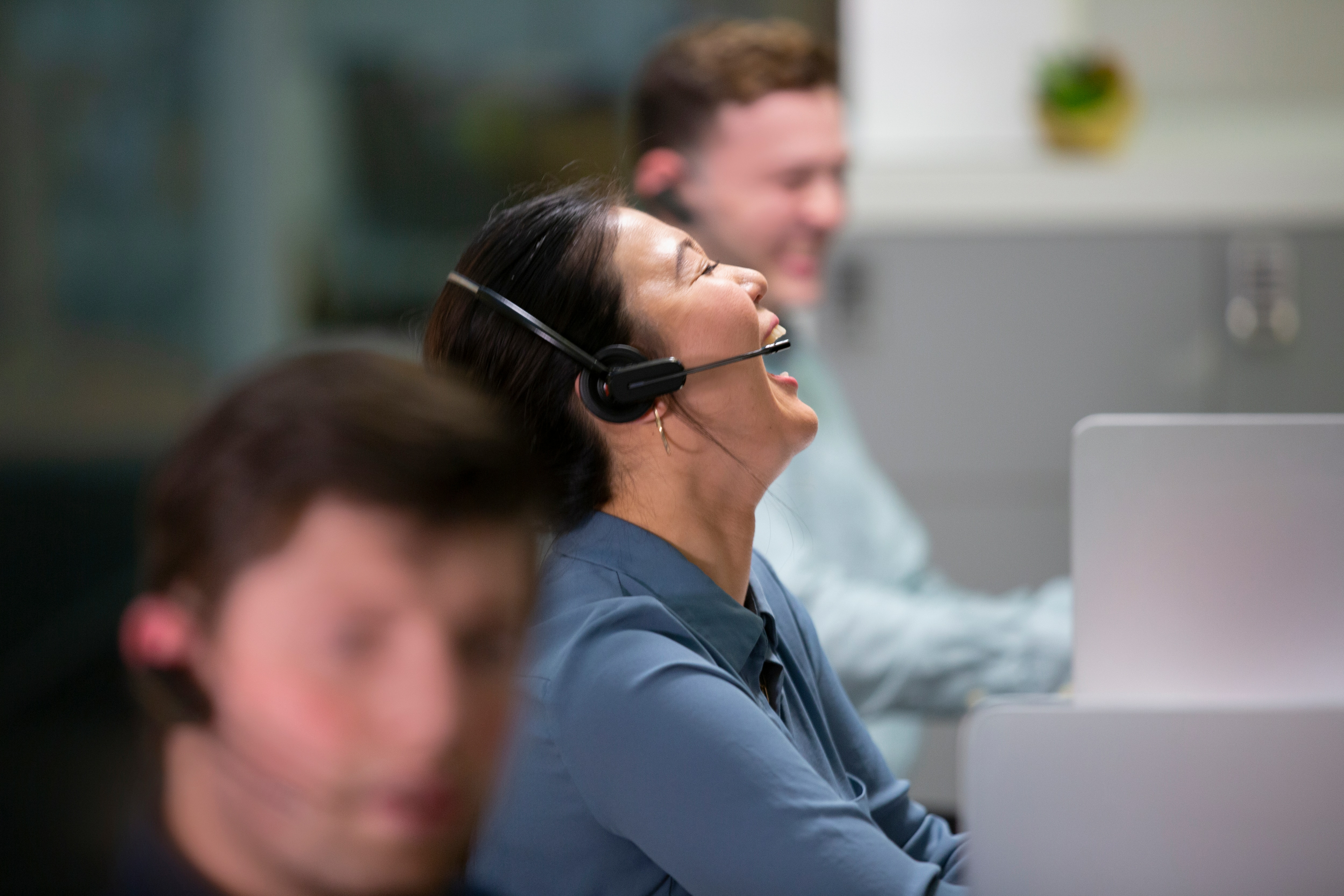 Tre persone ridono in un ufficio. Una donna indossa un auricolare.