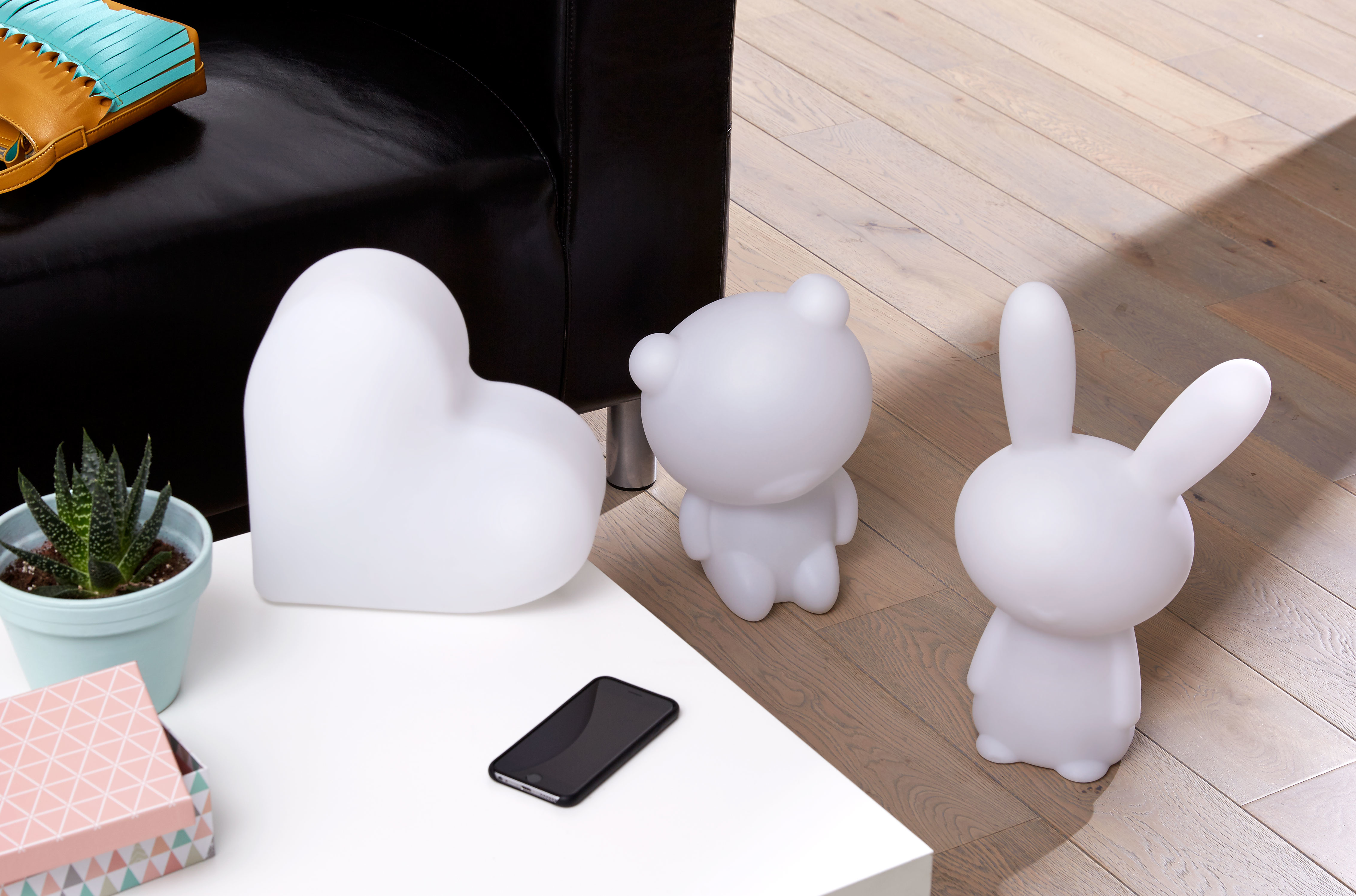 Białe lampy w kształcie serca, misia i królika na białym stole. Obecny jest również telefon i roślina.