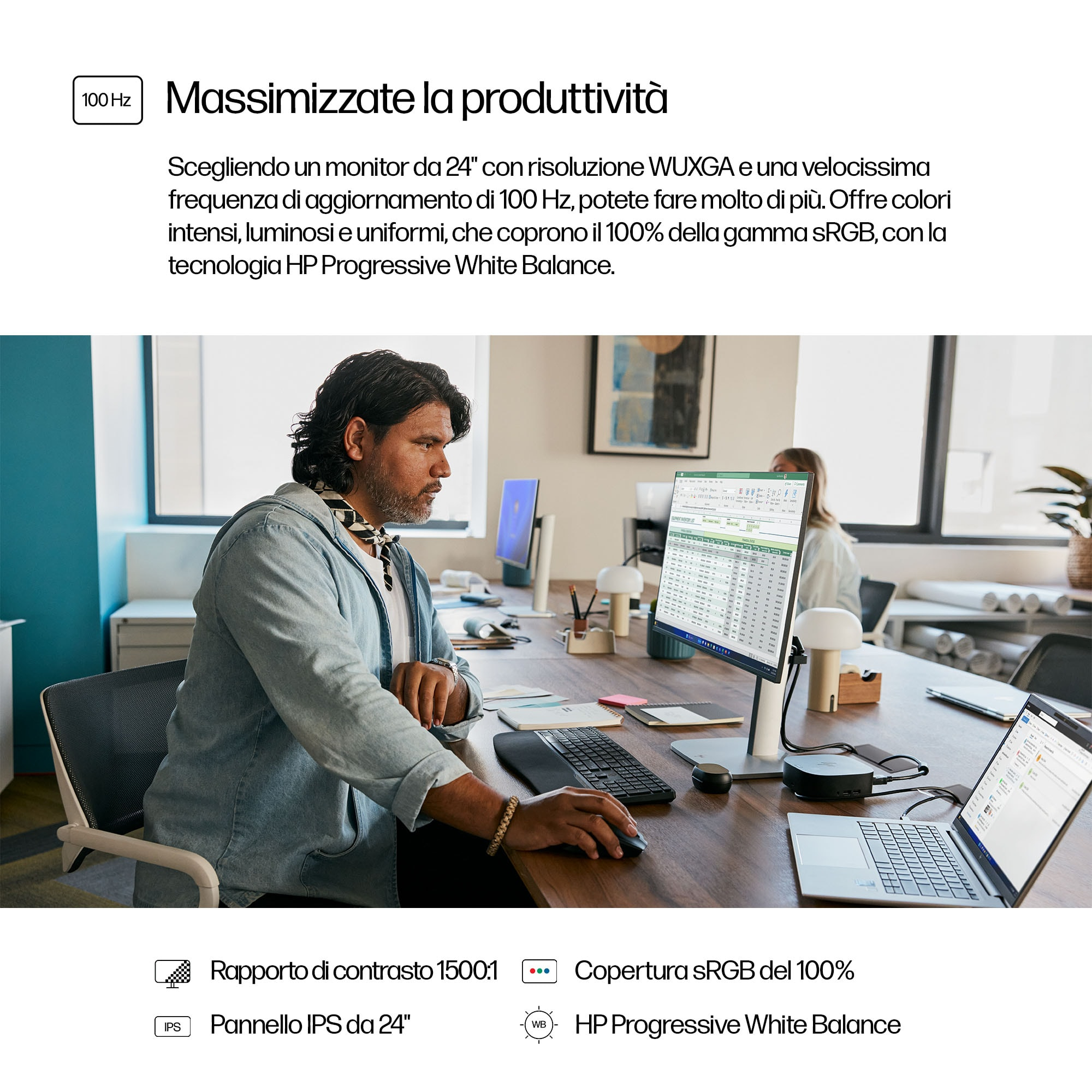 Mężczyzna pracuje na komputerze w biurze. Monitor wyświetla dane, a druga osoba siedzi.