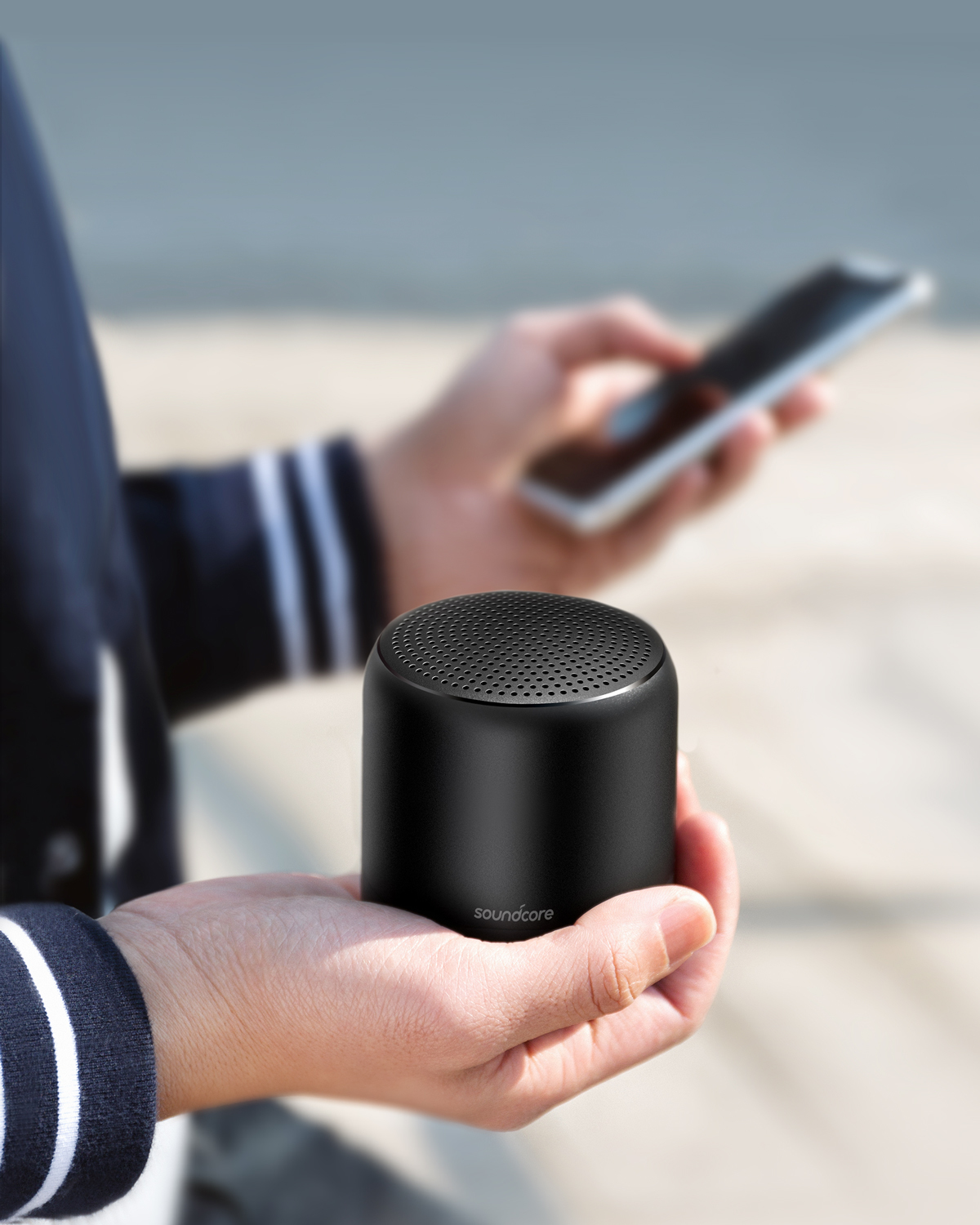 Osoba trzymająca mały czarny głośnik Soundcore i smartfona.