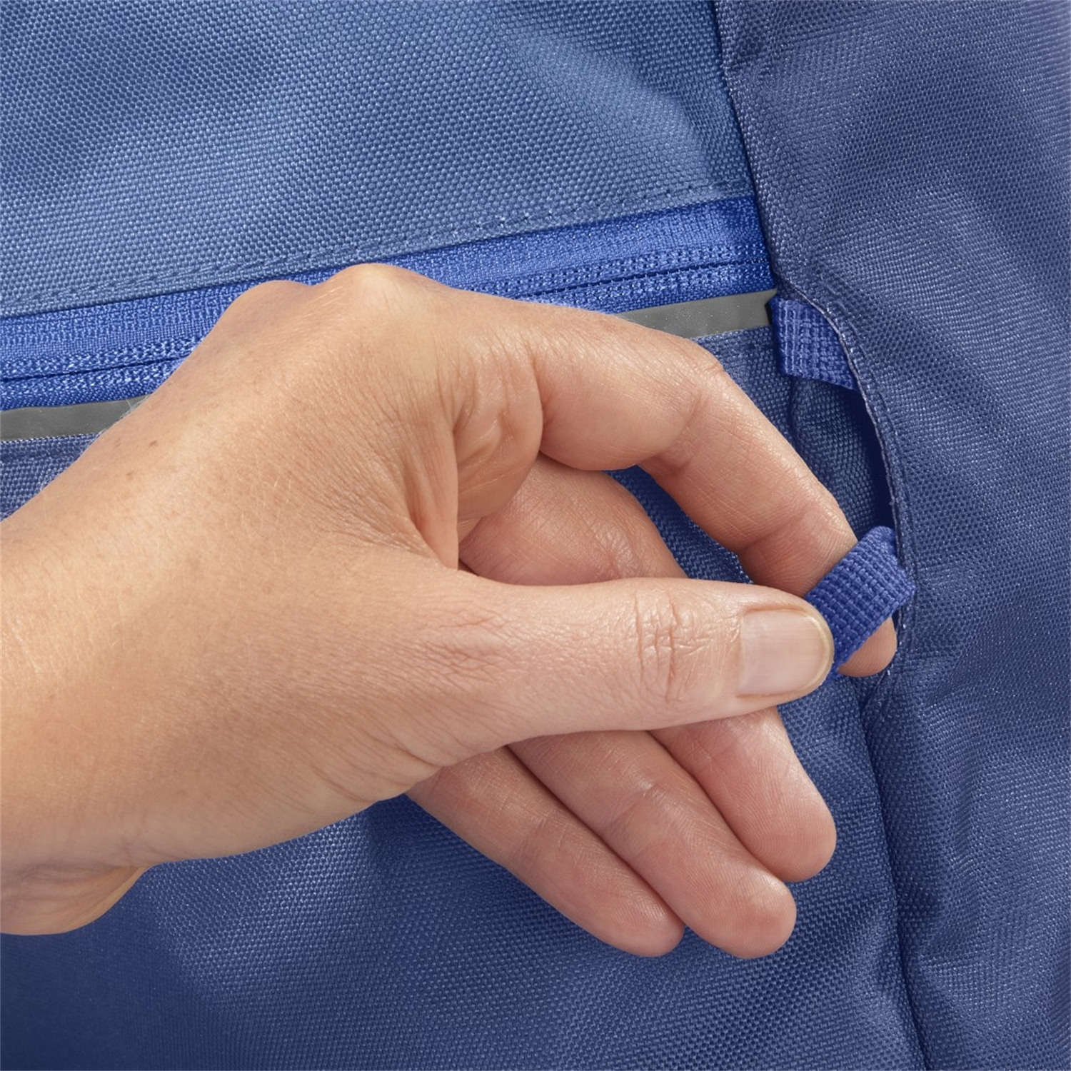 Hand zieht einen blauen Reißverschluss-Schieber an einer blauen Tasche.